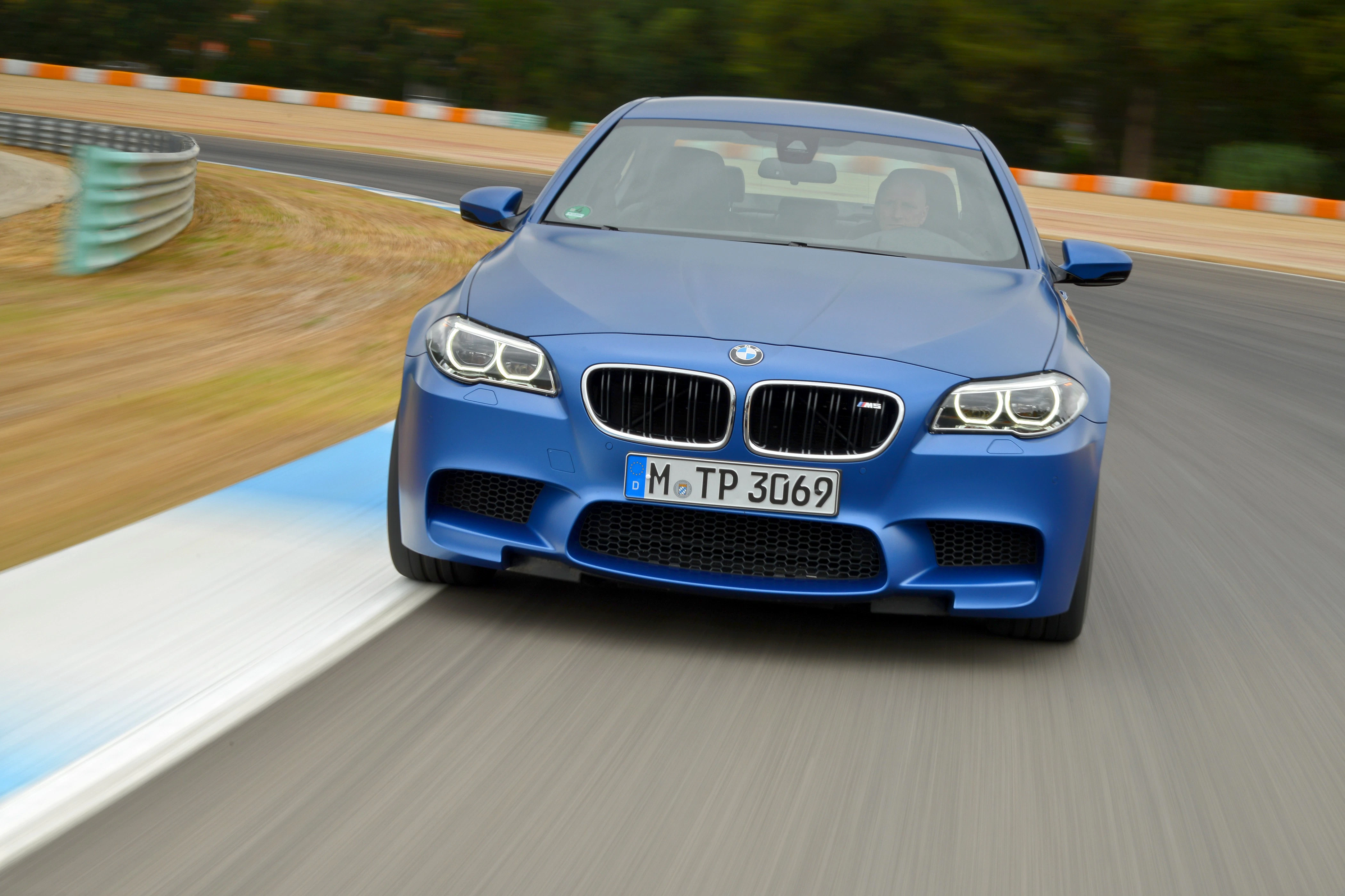 Blauer BMW fährt mit hoher Geschwindigkeit auf einer kurvigen Rennstrecke. Bäume und Streckenbegrenzung im Hintergrund.
