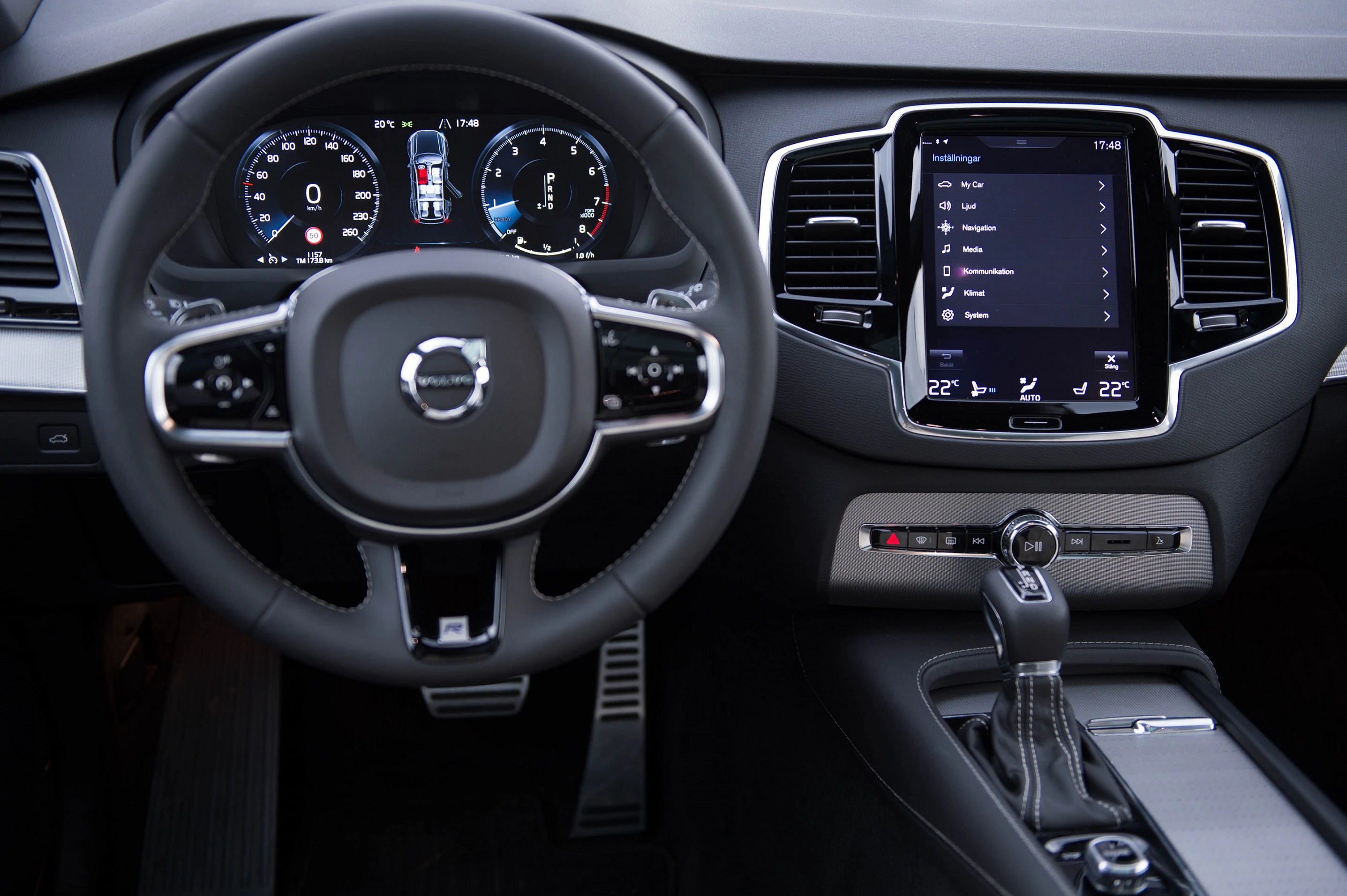 Lenkrad und digitales Armaturenbrett eines modernen Autos mit Touchscreen und Schalthebel. Anzeige von Geschwindigkeit und Navigationseinstellungen.
