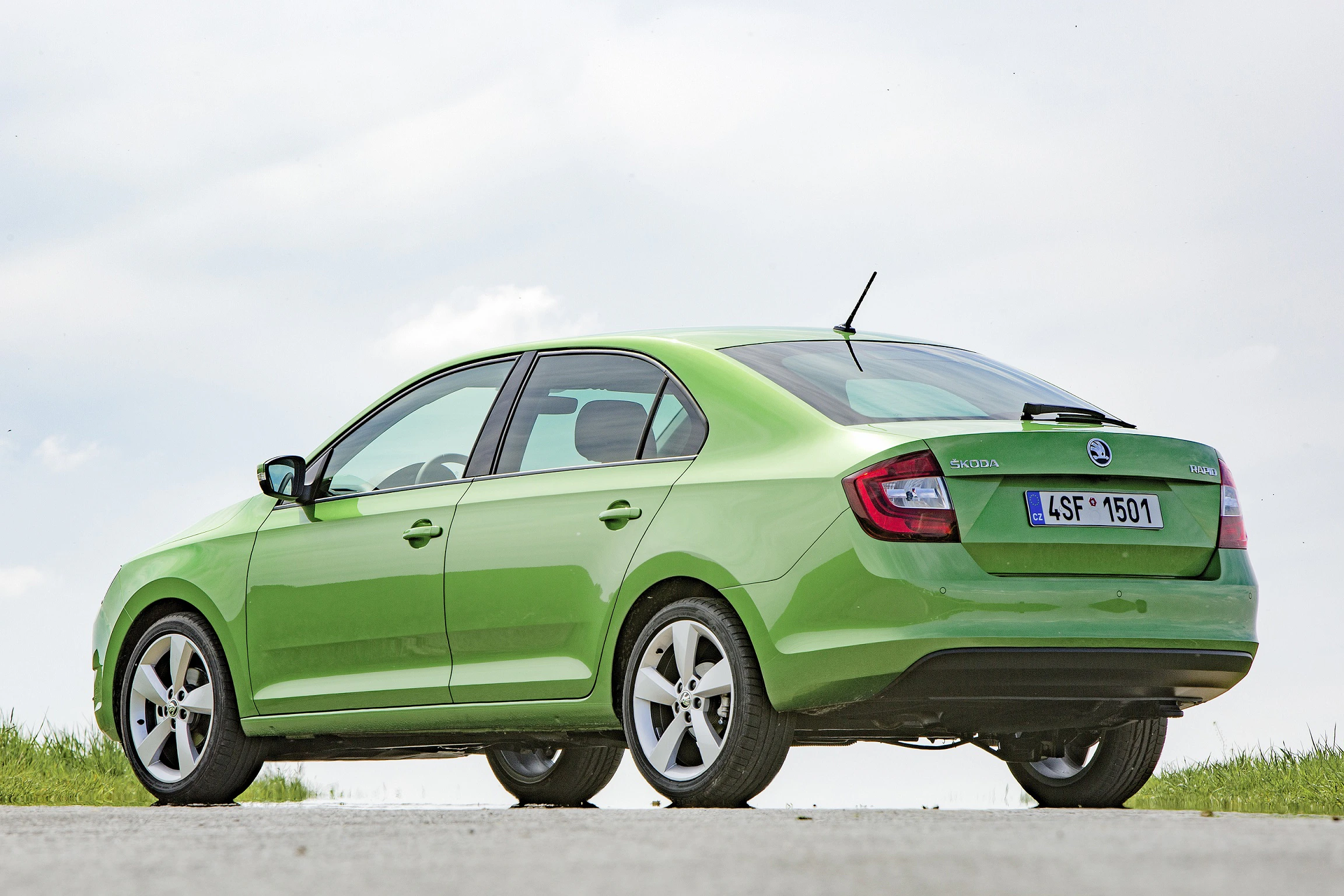 Grünes Auto (Skoda) auf einer Straße bei Tageslicht. Fahrzeug von der Seite und hinten sichtbar, mit klarem Himmel im Hintergrund.