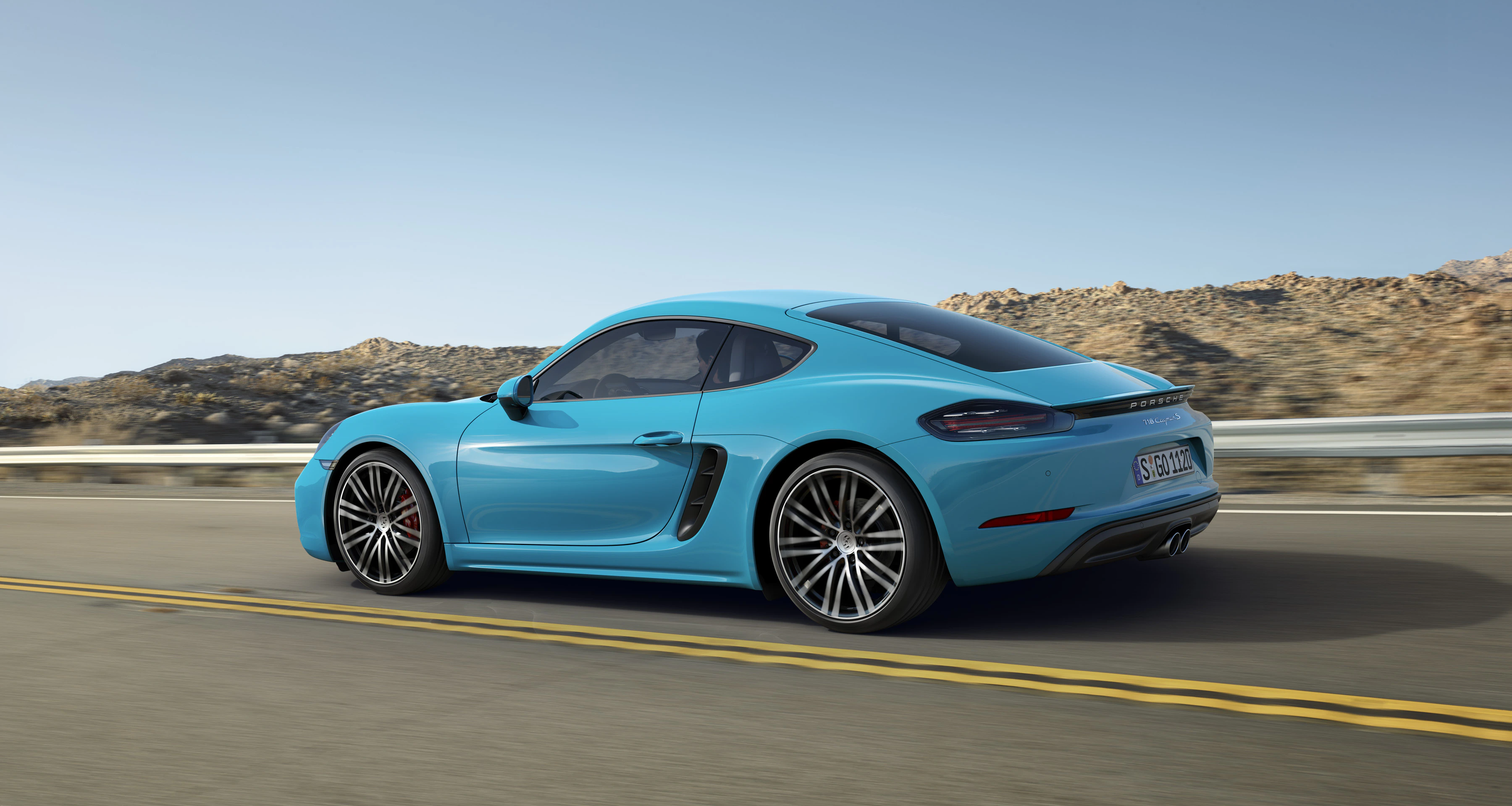Ein blauer Sportwagen fährt auf einer Straße durch eine wüstenartige Landschaft unter klarem Himmel.