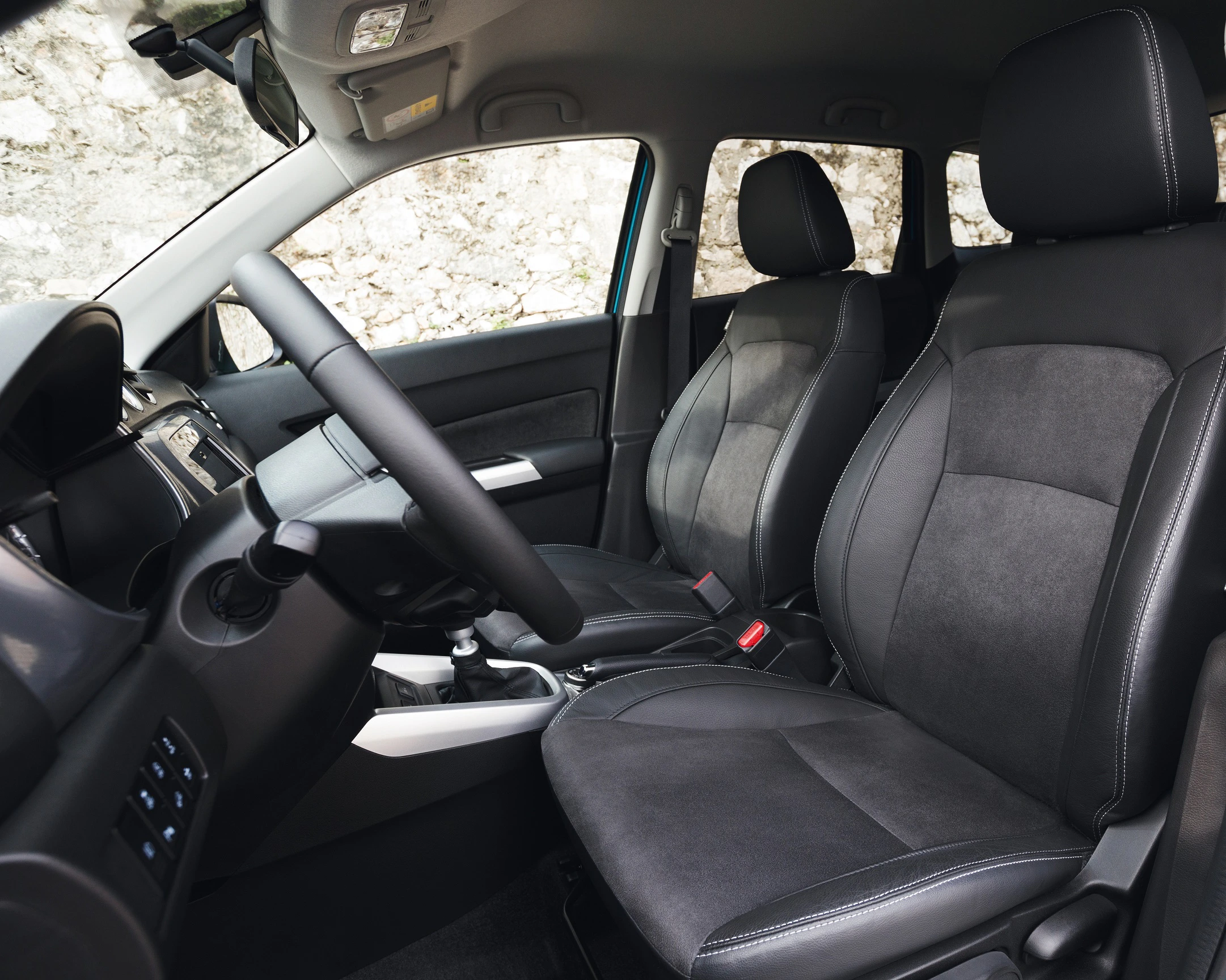 Innenraum eines Autos mit schwarzen Sitzen, einem Lenkrad, und einem Armaturenbrett. Die Sitze sind aus Leder und Stoff gefertigt.