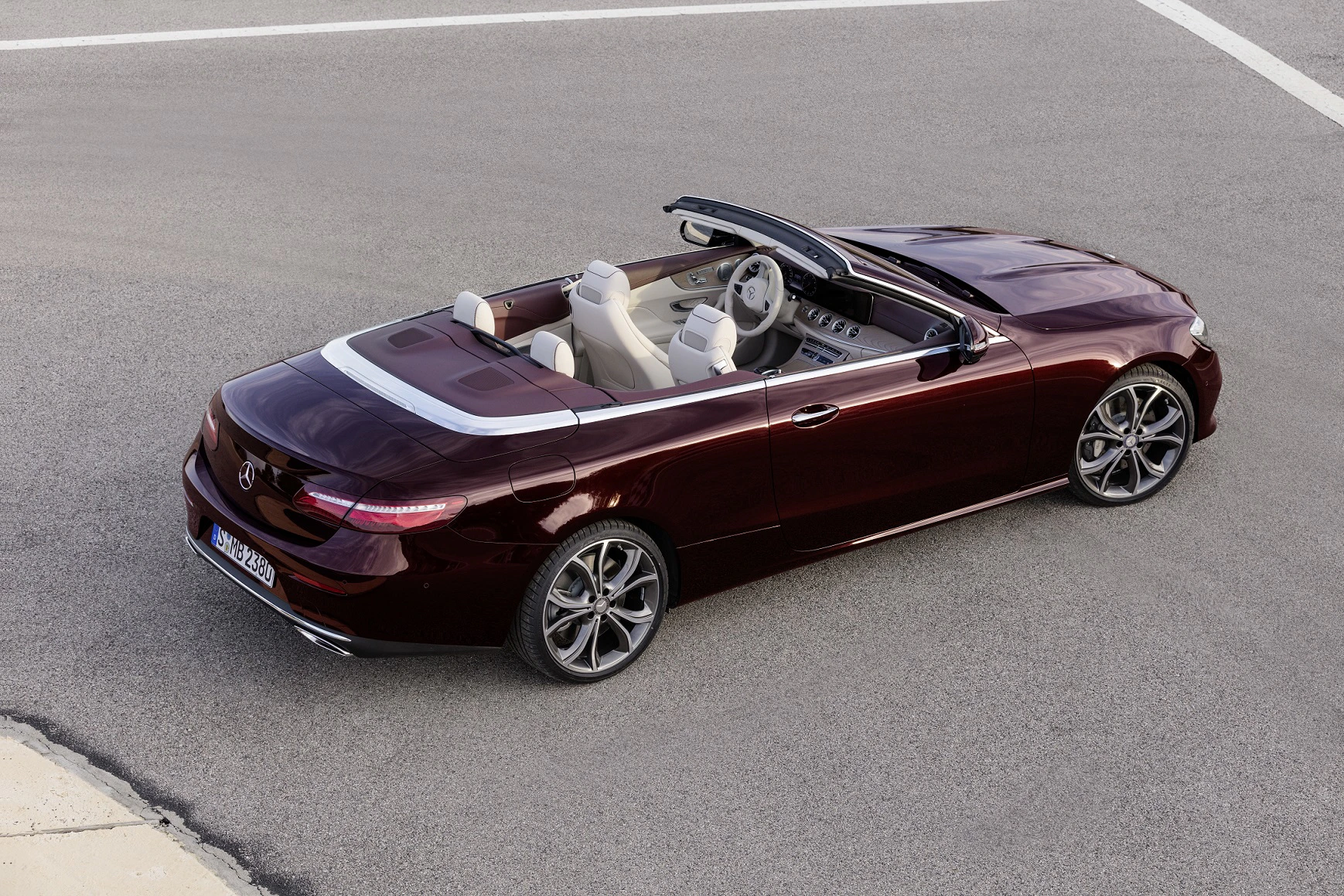 Weinrotes Cabriolet mit offenem Verdeck, stilvollem Innenraum und modernen Felgen, parkt auf grauem Asphalt.