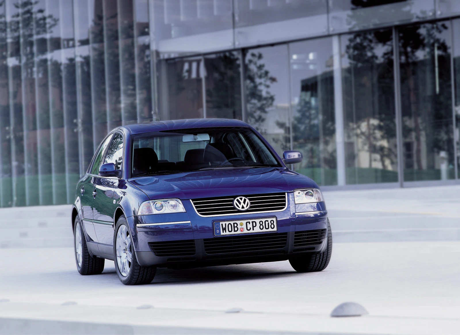 Blauer Volkswagen Passat vor moderner Glasfassade geparkt, Frontansicht.