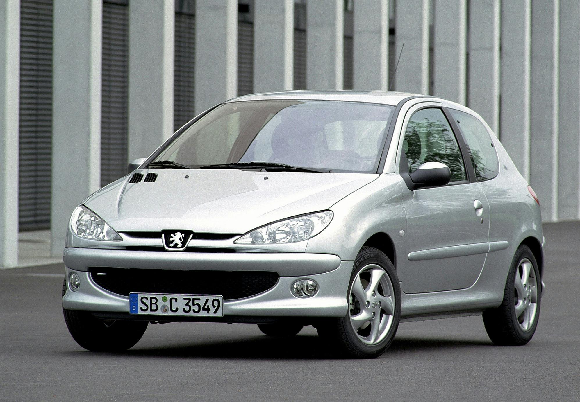 Silberner Peugeot 206 vor einem modernen Gebäude geparkt, Vorderansicht. Auto mit deutschen Kennzeichen auf grauem Asphalt.
