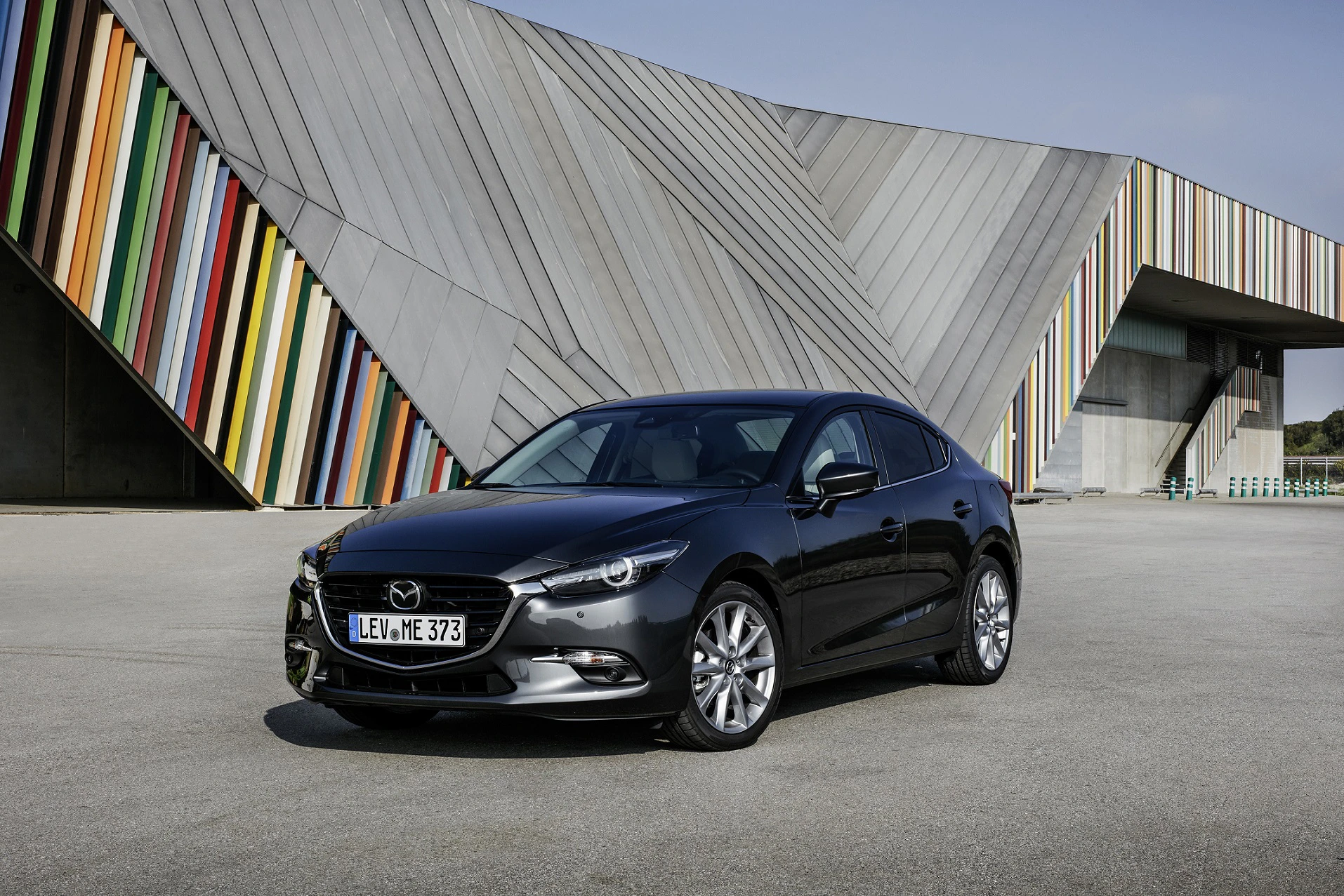 Schwarzer Mazda vor modernem Gebäude mit bunten Streifen und geometrischen Formen.