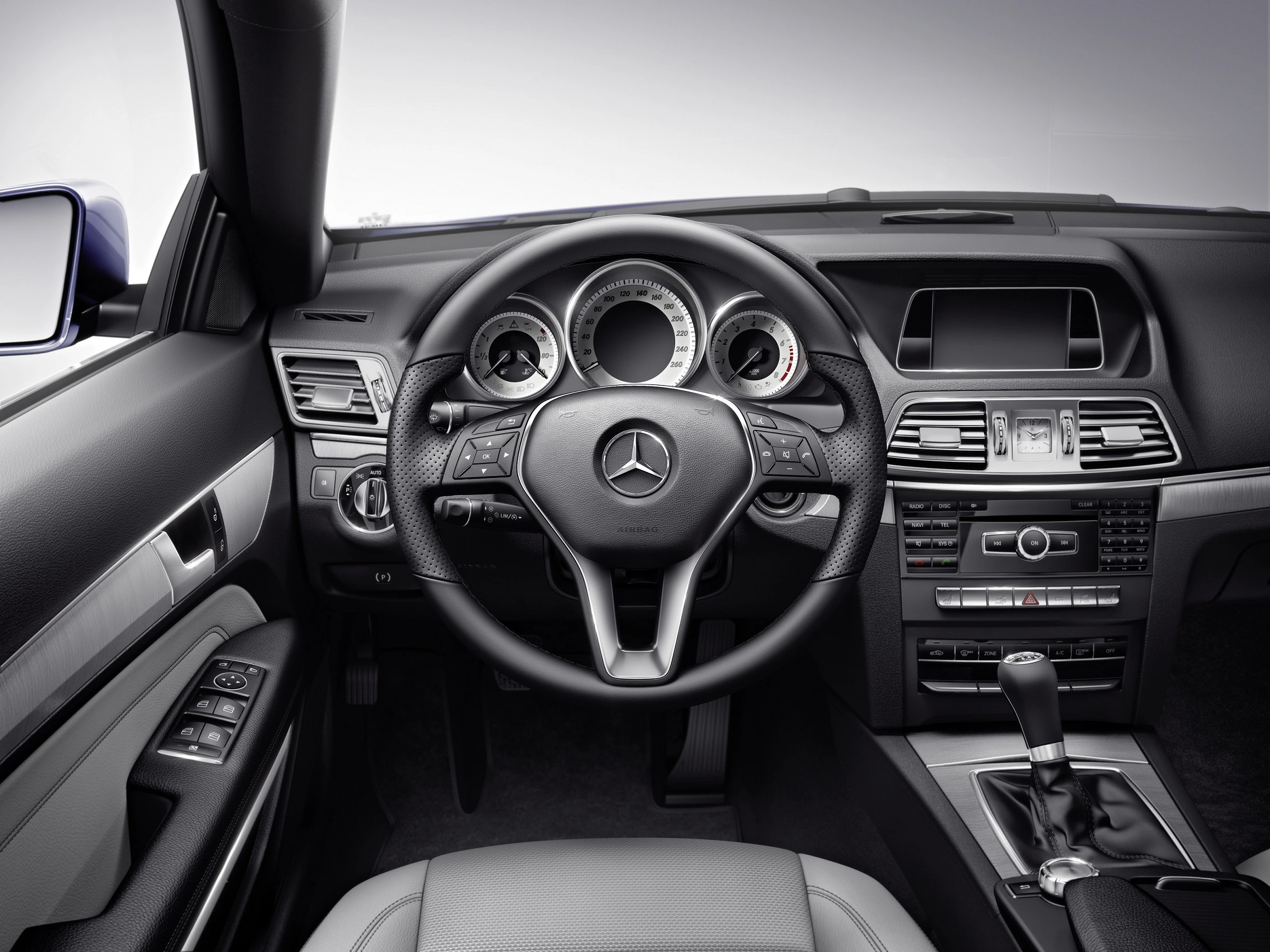 Innenraum eines Mercedes-Benz mit Fokus auf das Lenkrad und das Armaturenbrett; gut sichtbare Instrumententafel und Schalthebel.