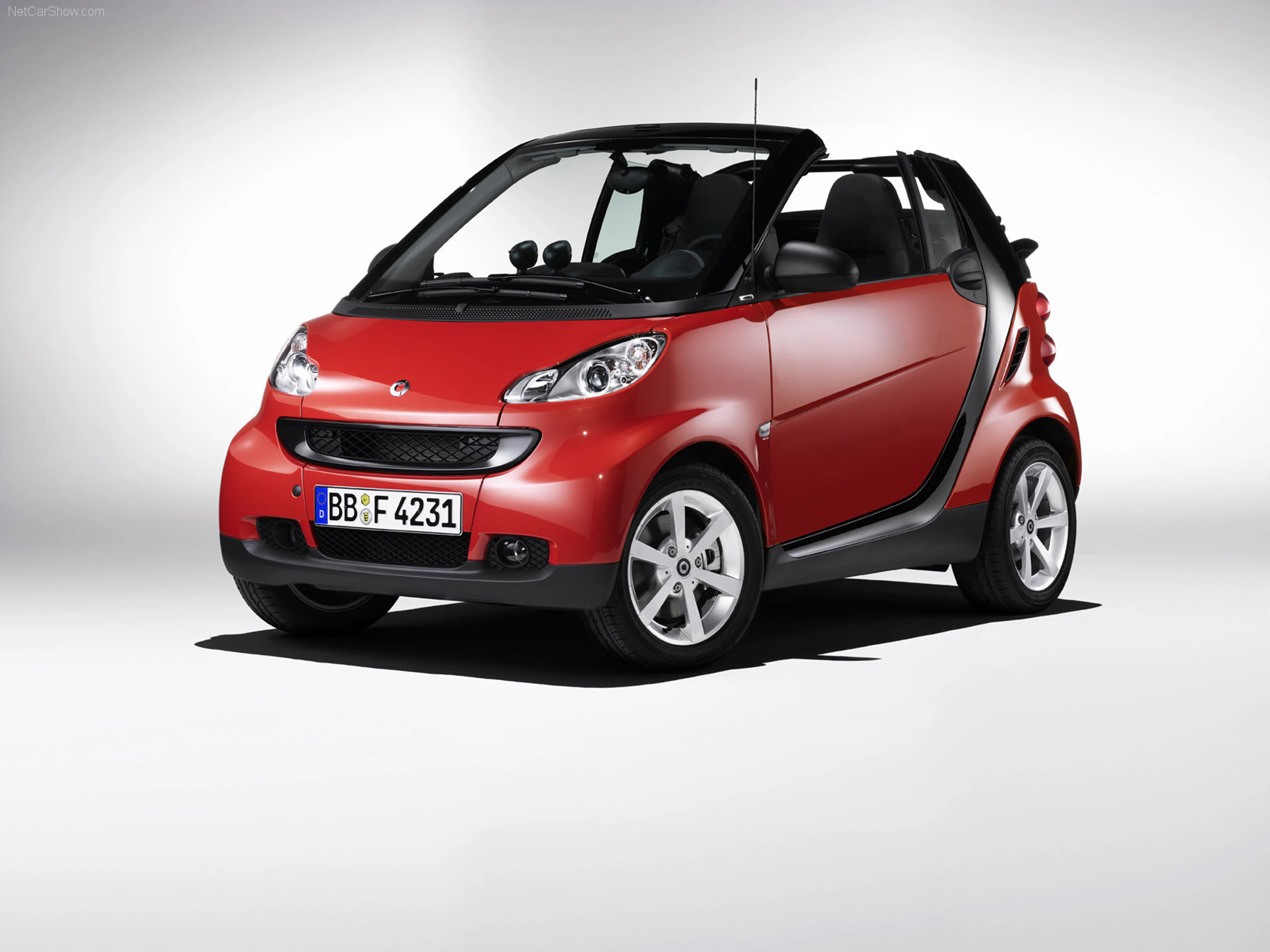 Rotes Smart Cabrio Auto vor weißem Hintergrund, schrägdraufsicht, mit offenem Verdeck und sichtbarem Nummernschild.