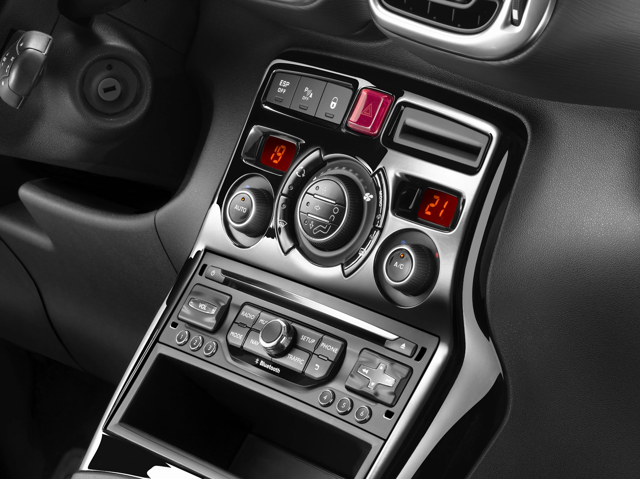 Mittelkonsole eines Autos mit Klimasteuerung, Radioknöpfen und Display. Zeigt Temperatur von 19°C und 21°C. Schwarz-silbernes Design.