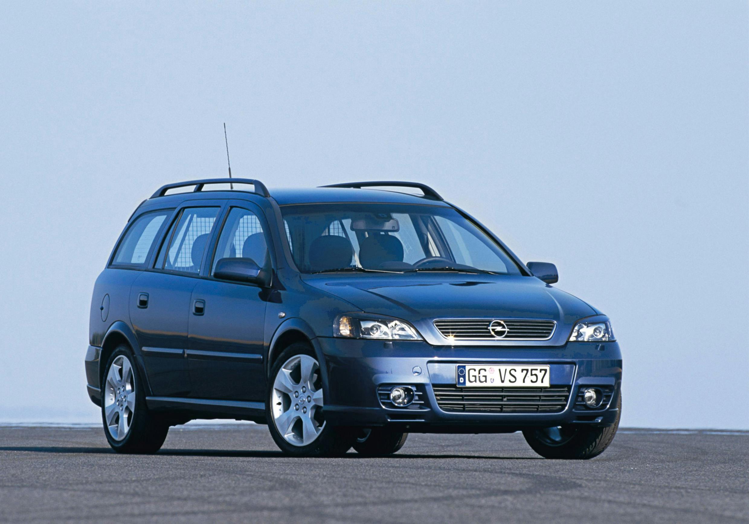 Dunkelblauer Opel Kombi auf freier Fläche, von schräg vorne fotografiert. Klarer Himmel im Hintergrund.