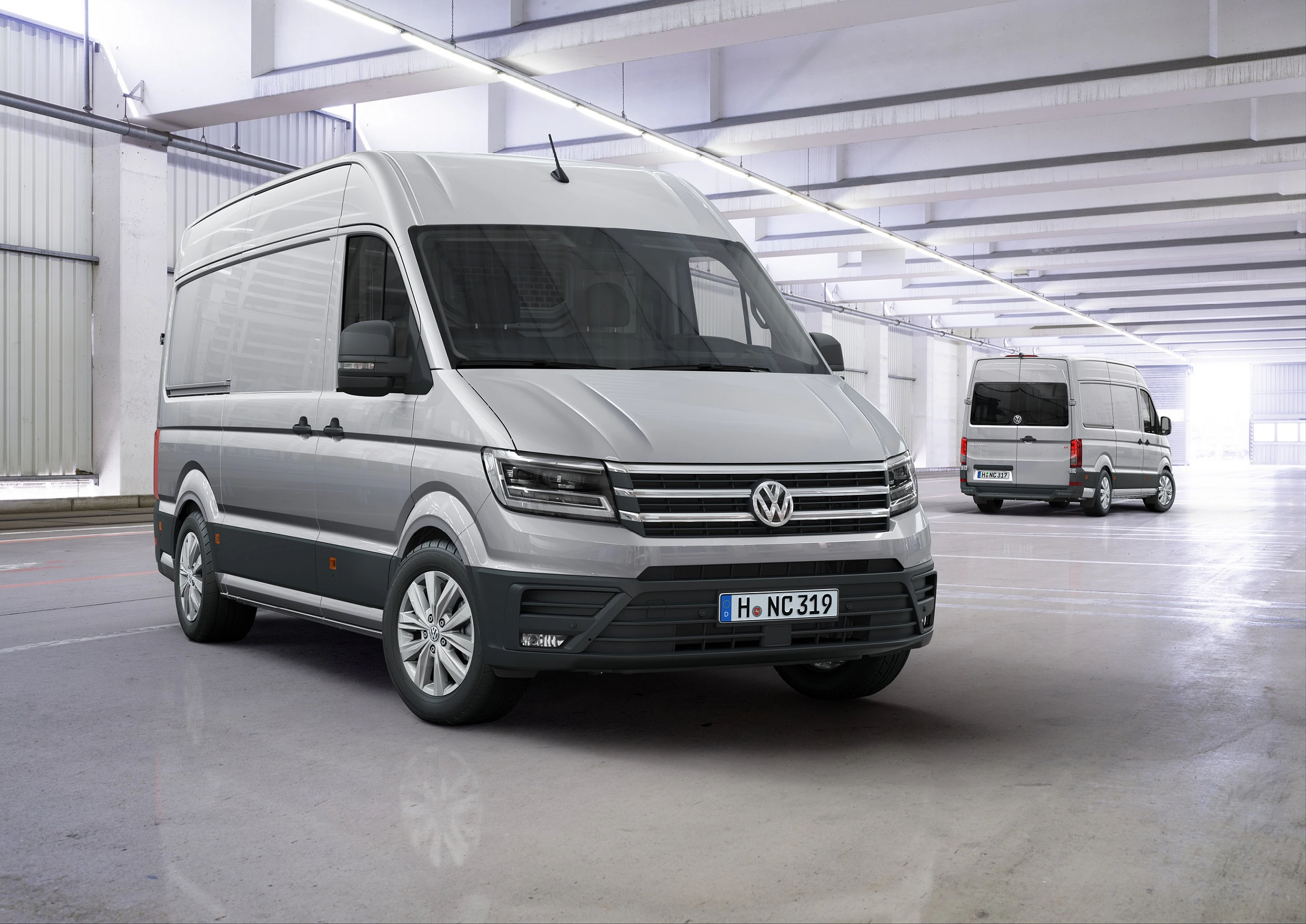 Zwei silberne Transporter in einer modernen, hellen Garage. Beide Fahrzeuge sind von Volkswagen.