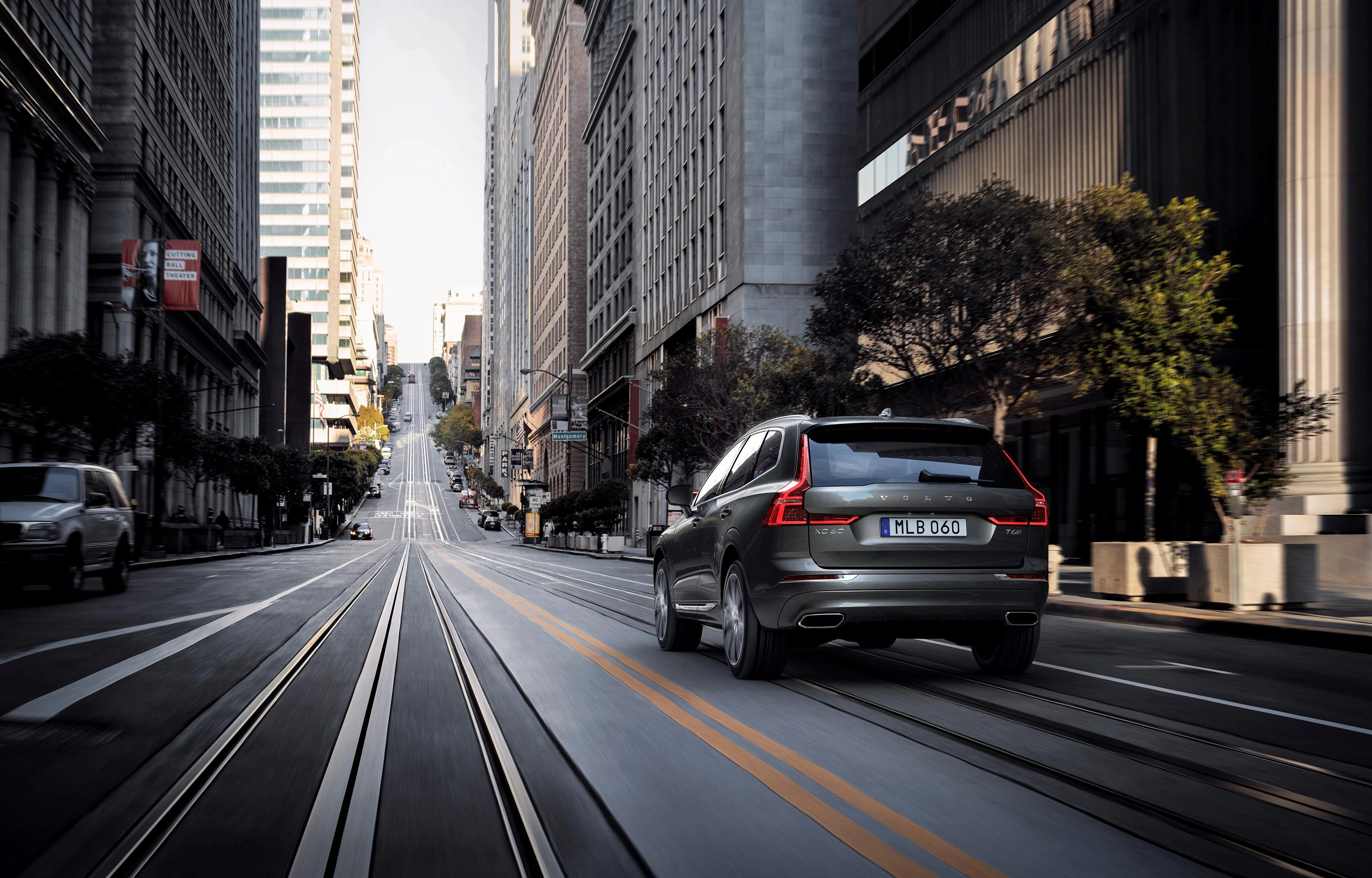 Ein grauer SUV fährt eine steile, leere Stadtstraße entlang, umgeben von modernen Hochhäusern.