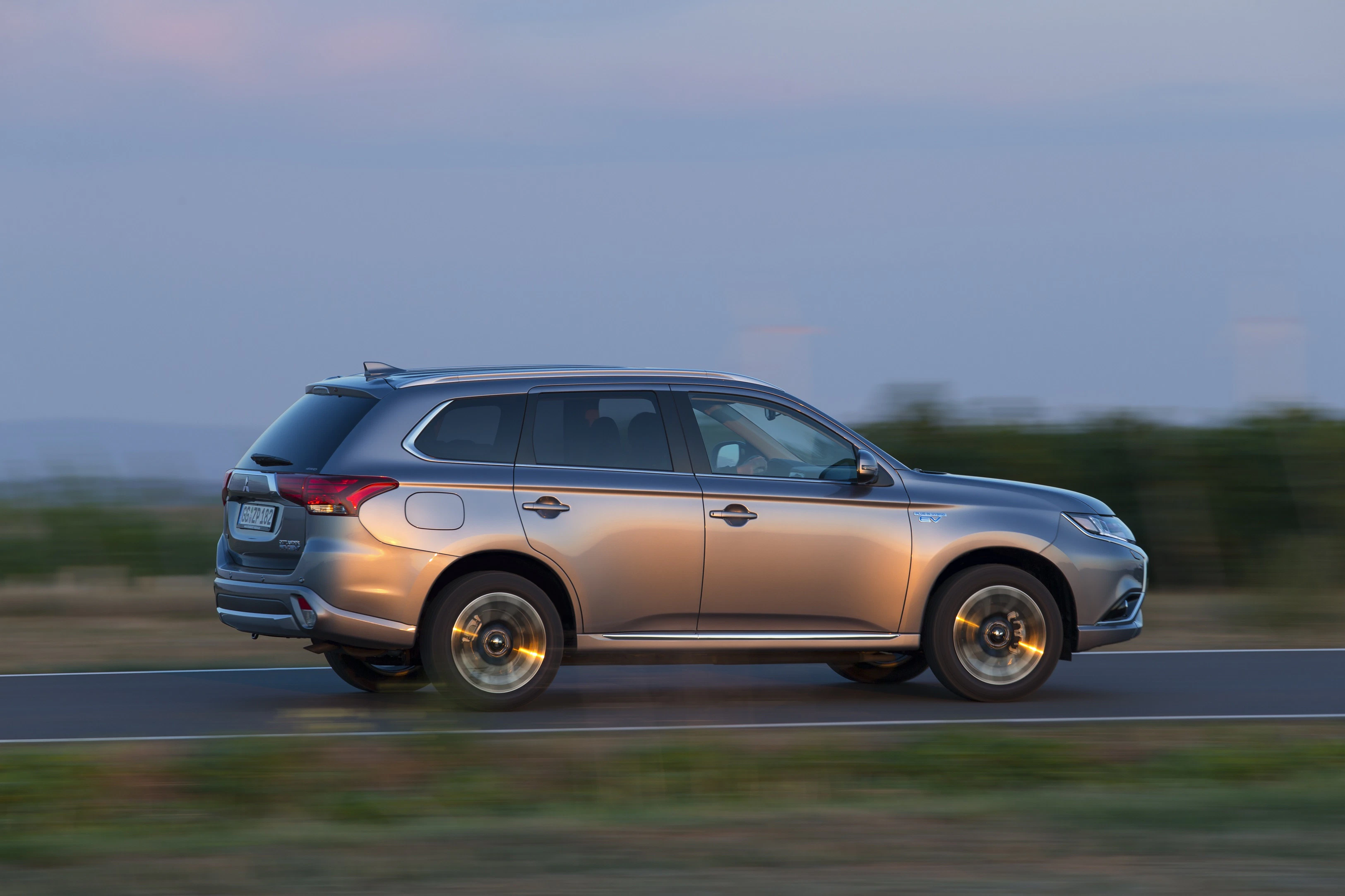 Silbernes SUV fährt bei Sonnenuntergang auf einer Landstraße. Bewegungsunschärfe zeigt Geschwindigkeit. Im Hintergrund Natur.
