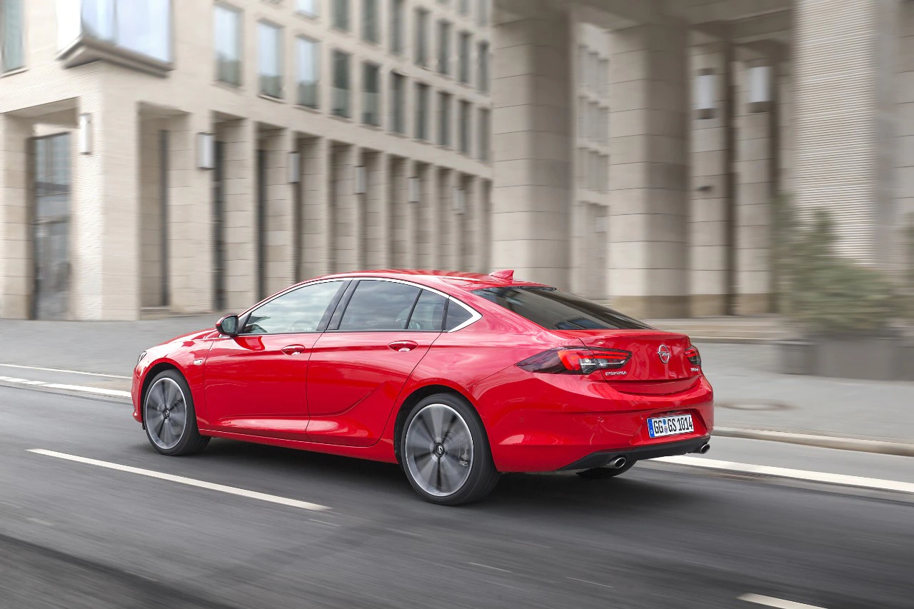 Rotes Auto fährt schnell auf einer urbanen Straße; moderne Gebäude im Hintergrund.