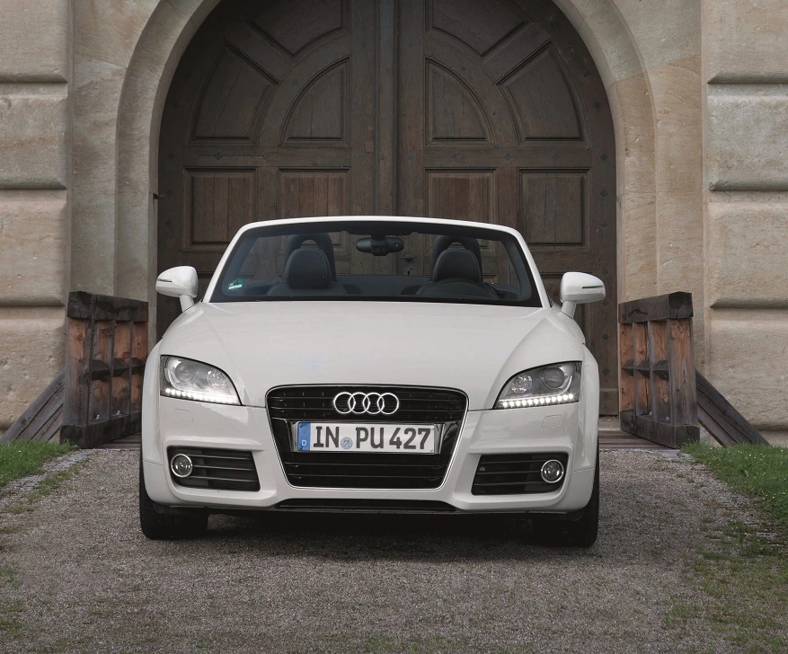 Weißes Audi-Cabriolet steht vor einem steinernen Torbogen. Das Auto hat das Verdeck geöffnet und einen bayerischen Kennzeichen.