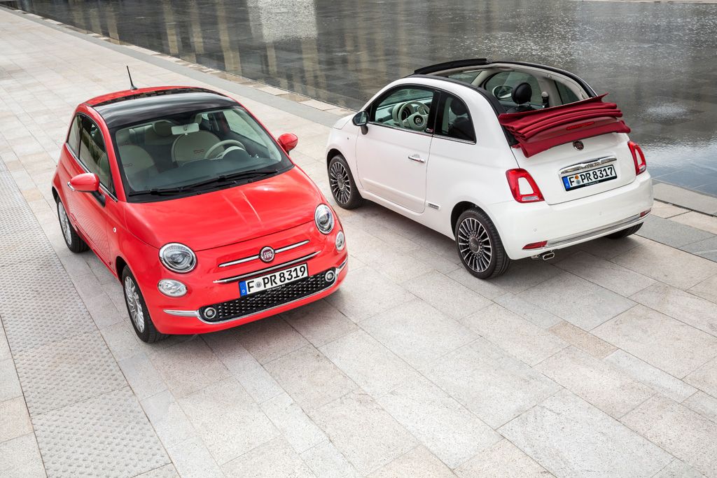 Zwei Fiat 500 in Rot und Weiß, parken nebeneinander auf einem gepflasterten Platz. Der weiße Wagen hat ein geöffnetes Stoffverdeck.