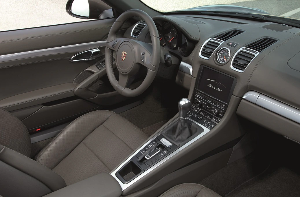 Innenraum eines Porsche mit Ledersitzen, Schalthebel, Lenkrad und Bordcomputer. Modernes Design in Grautönen.