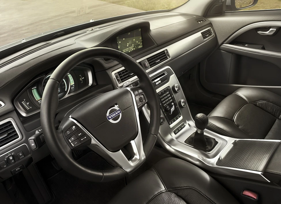 Innenraum eines Autos mit schwarzem Leder, Lenkrad mit Volvo-Logo, Schalthebel und zentralem Display am Armaturenbrett.