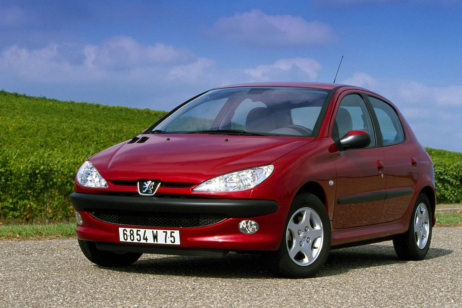 Rotes Auto auf einer Landstraße vor einem grünen Feld und blauem Himmel. Fünf Türen, runde Scheinwerfer und silberne Felgen.