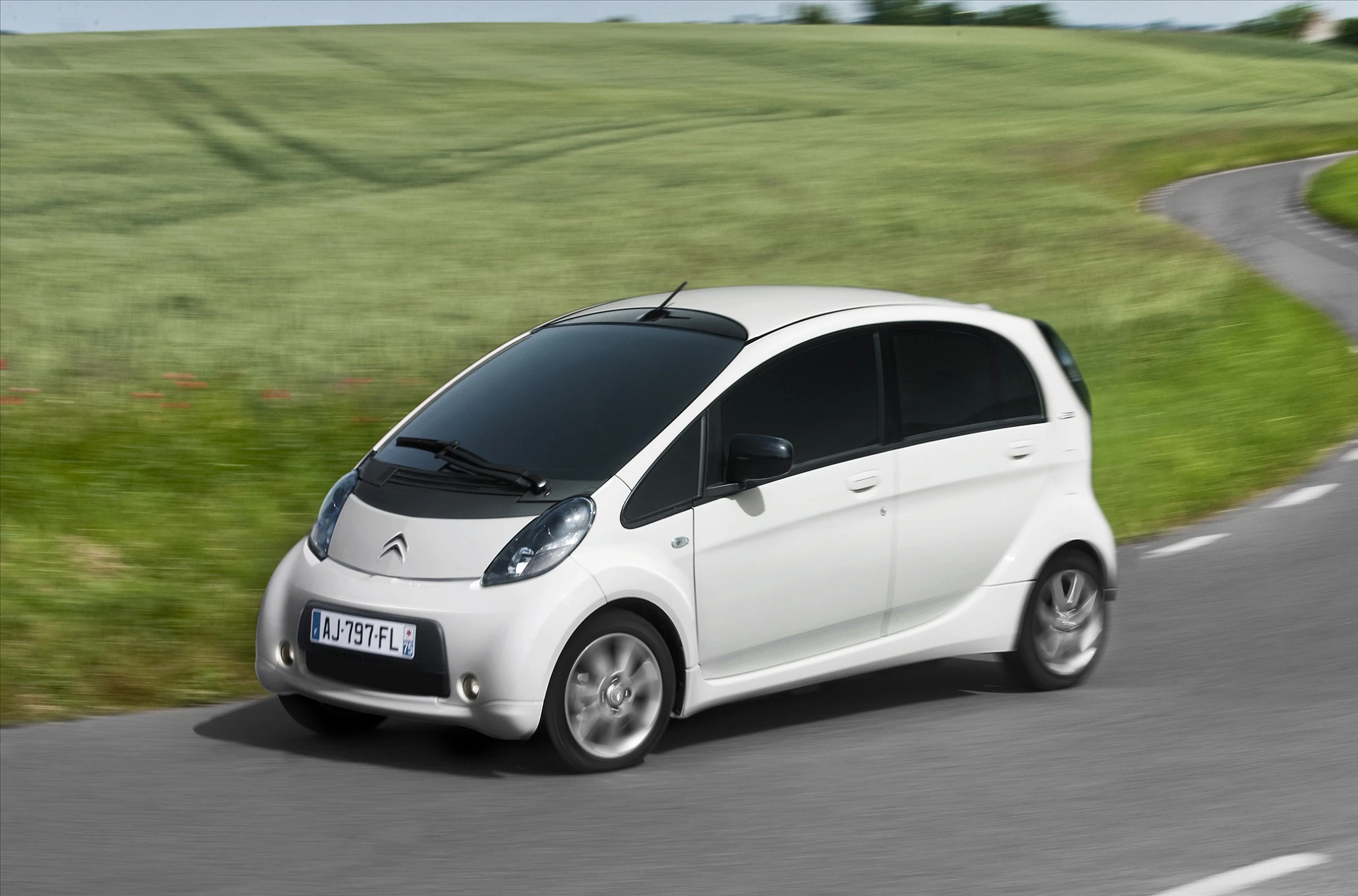 Weißer Citroën C-Zero fährt auf einer windigen Landstraße durch grüne Felder.