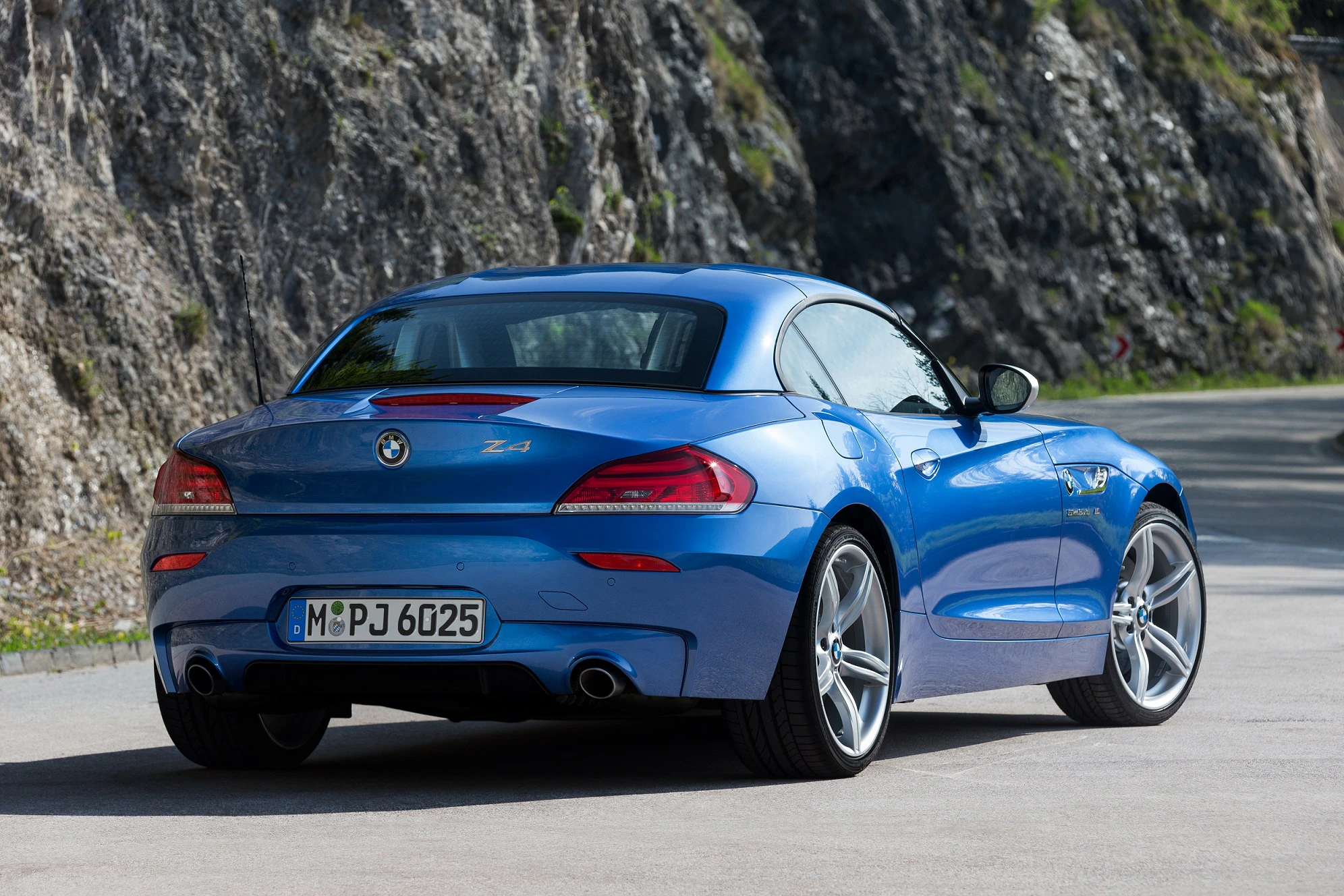 Blauer BMW Z4 auf einer Bergstraße, von hinten fotografiert. Sportliches Design mit geschlossenen Verdeck und Felsen im Hintergrund.