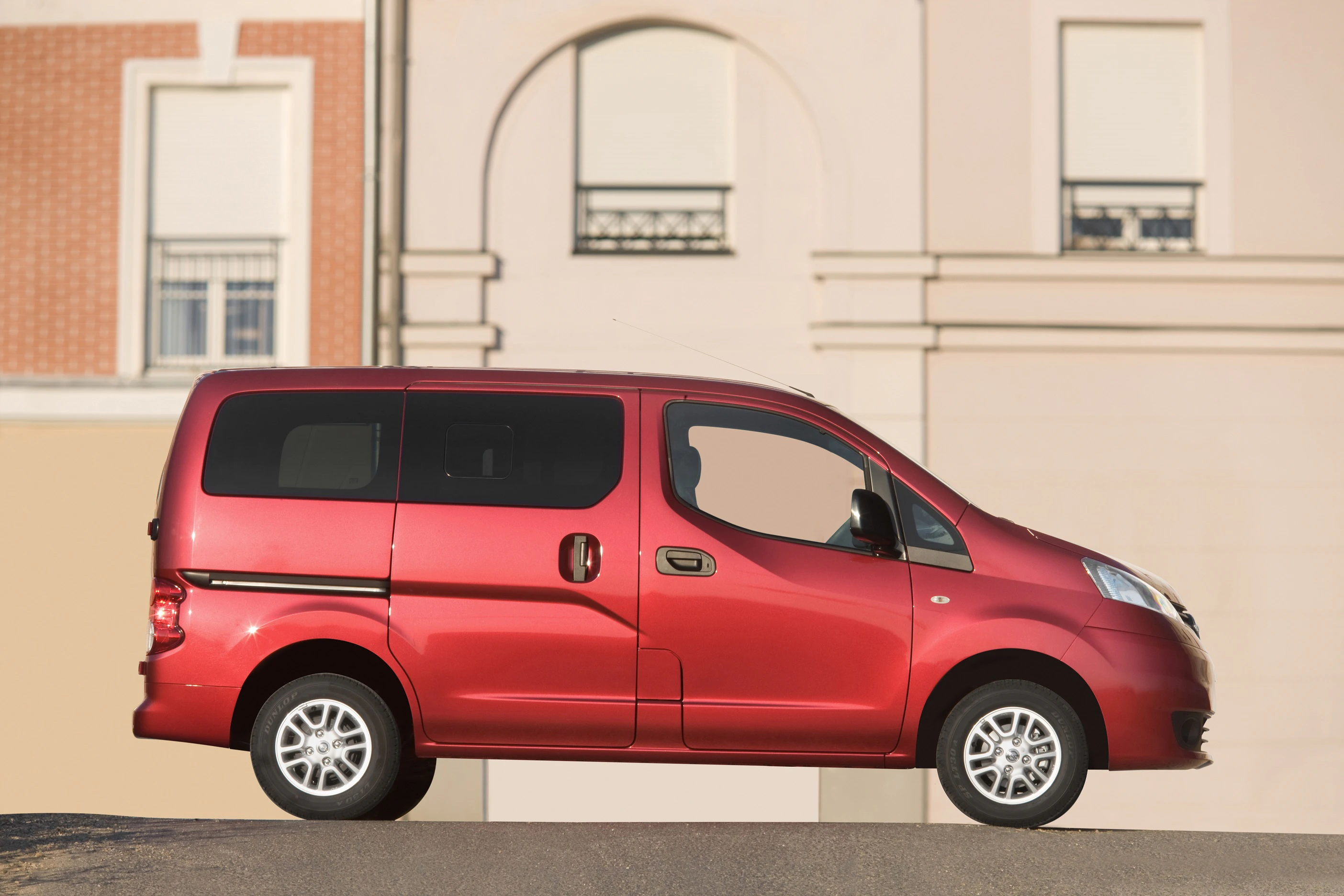 Roter Minivan steht vor einem beige-farbenen Gebäude mit einem großen Fenster und einer gewölbten Form.