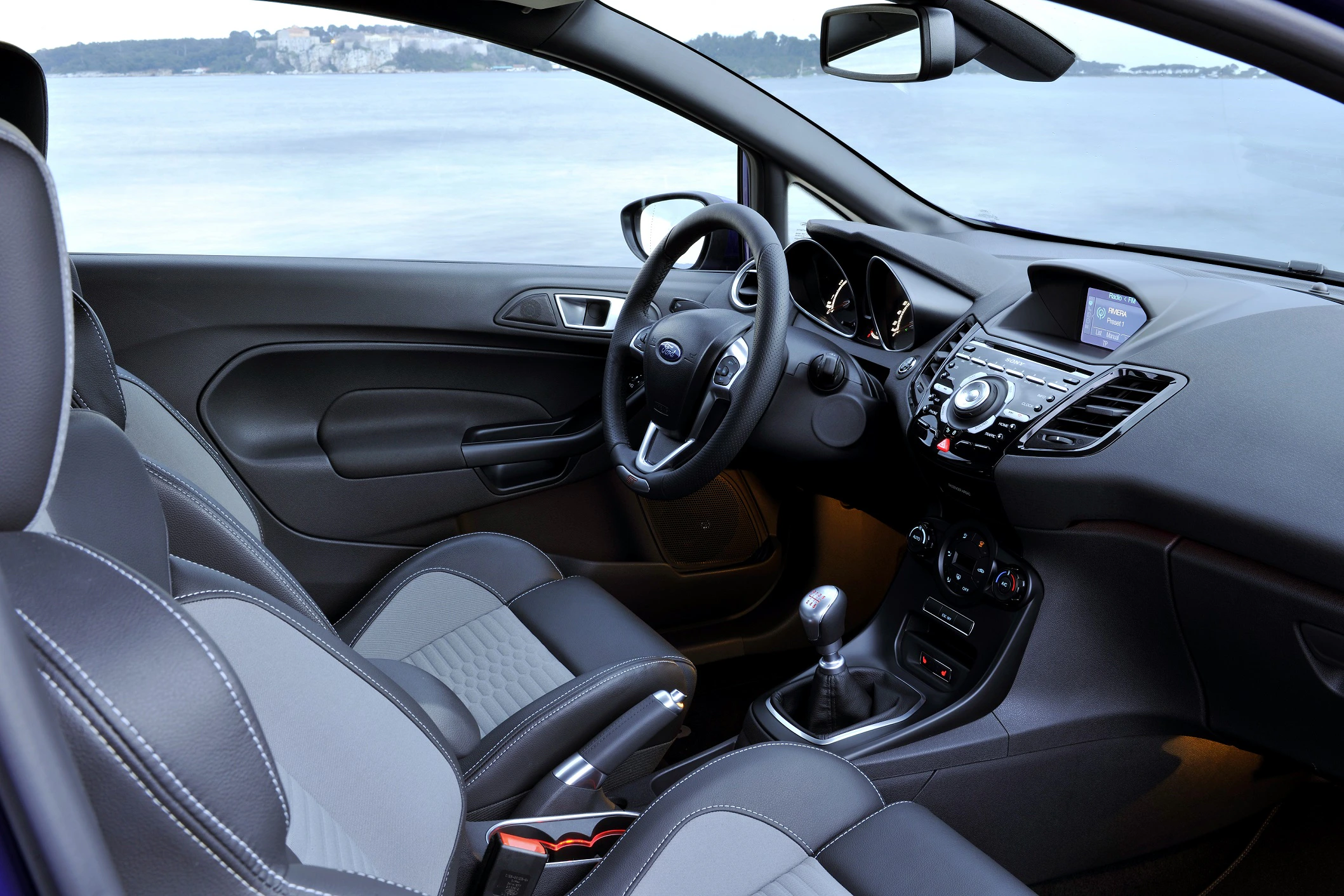 Innenraum eines modernen Autos mit schwarzem Lederinterieur und Schaltgetriebe, Blick auf Lenkrad und Armaturenbrett.