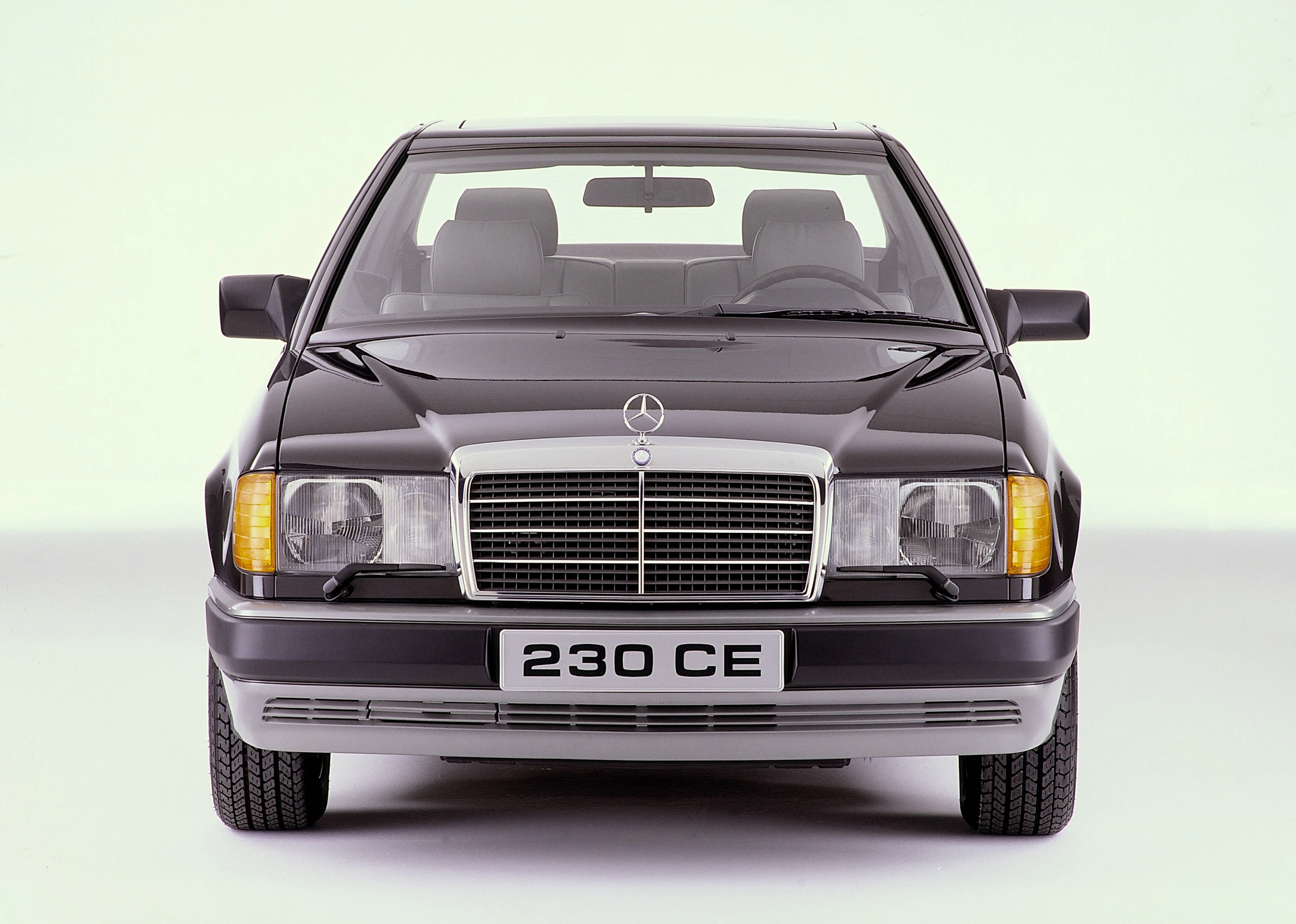 Frontansicht eines klassischen schwarzen Mercedes-Benz 230 CE mit charakteristischem Kühlergrill und rechteckigen Scheinwerfern.