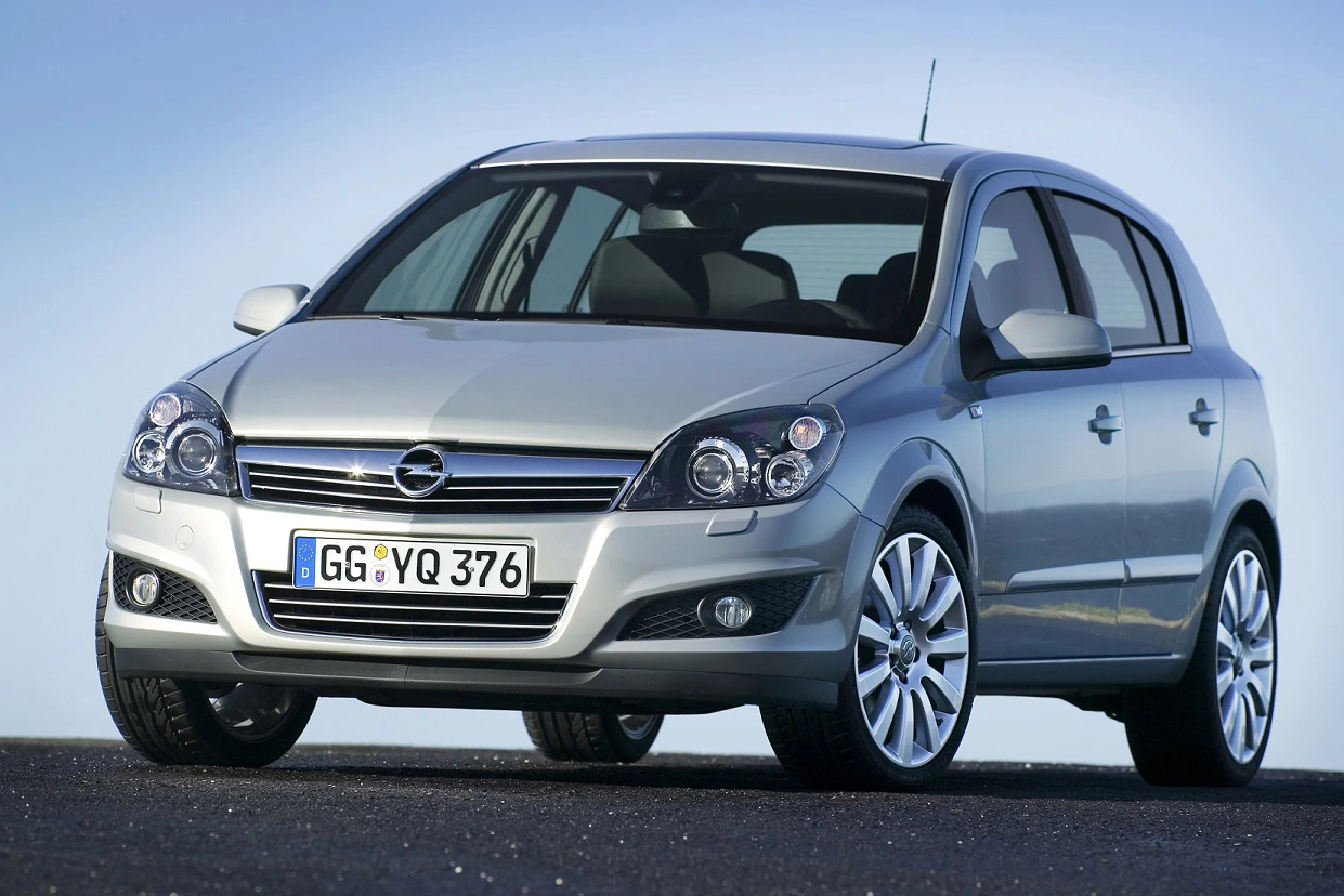 Silberner Opel Astra, viertürig, auf schwarzem Asphalt stehend vor blauem Himmel. Deutsche Nummernschilder.