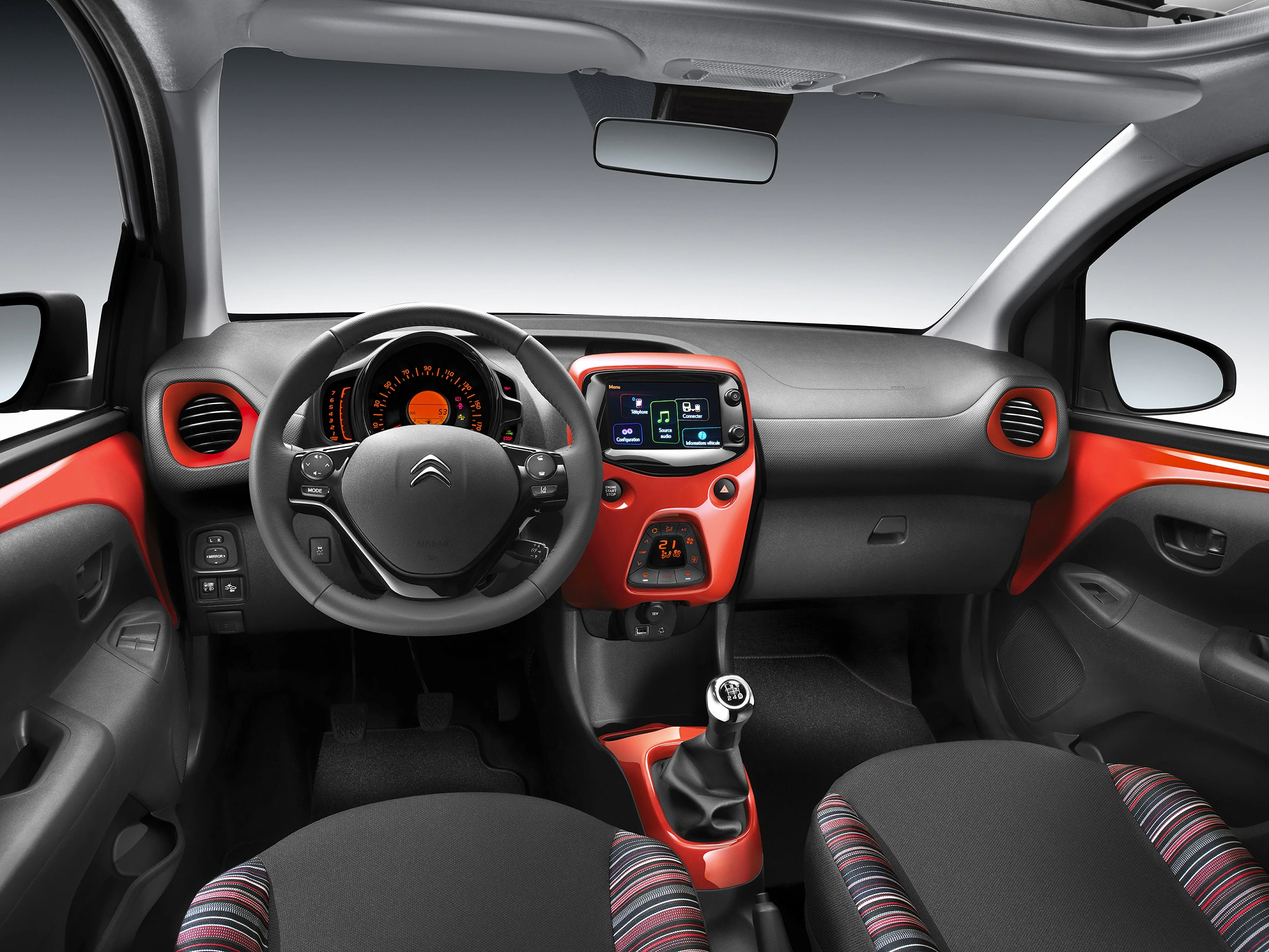 Innenraum eines Autos mit rot-schwarzem Cockpit, multifunktionalem Lenkrad und modernem Touchscreen-Display. Manuelles Schaltgetriebe sichtbar.