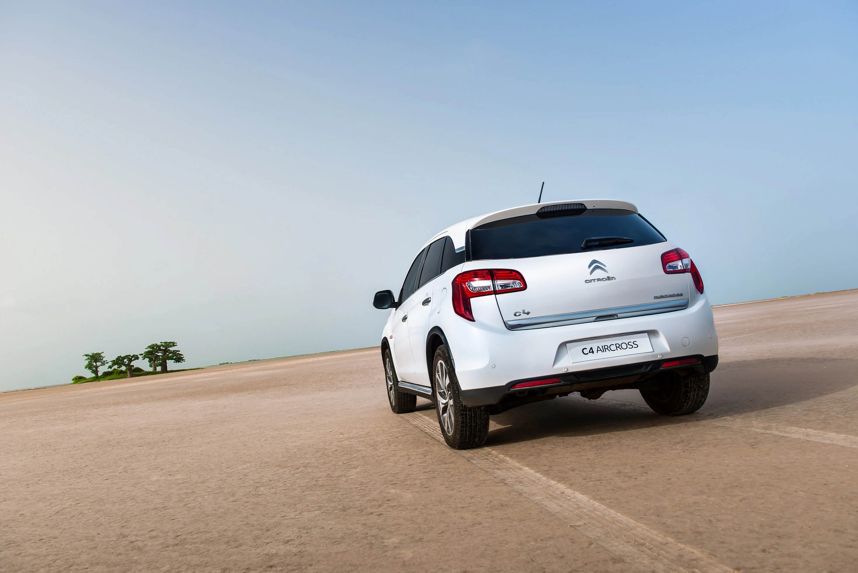 Ein weißer Citroën C4 Aircross fährt auf einer weiten, trockenen Landschaftsstraße, unter einem klaren blauen Himmel.