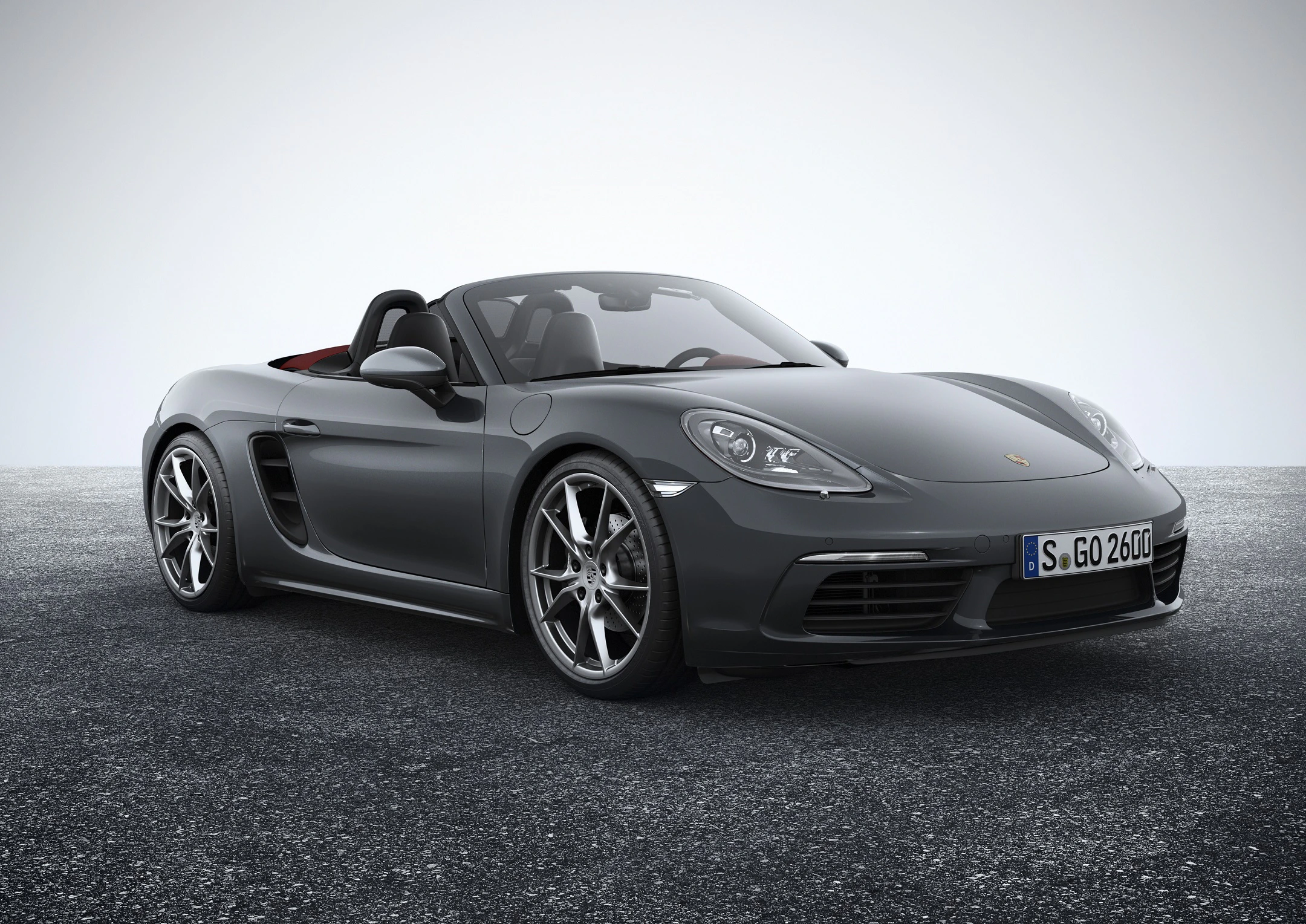 Graues Cabriolet mit geöffnetem Verdeck auf grauem Asphalt. Frontseitige Ansicht zeigt sportliches Design und glänzende Felgen.