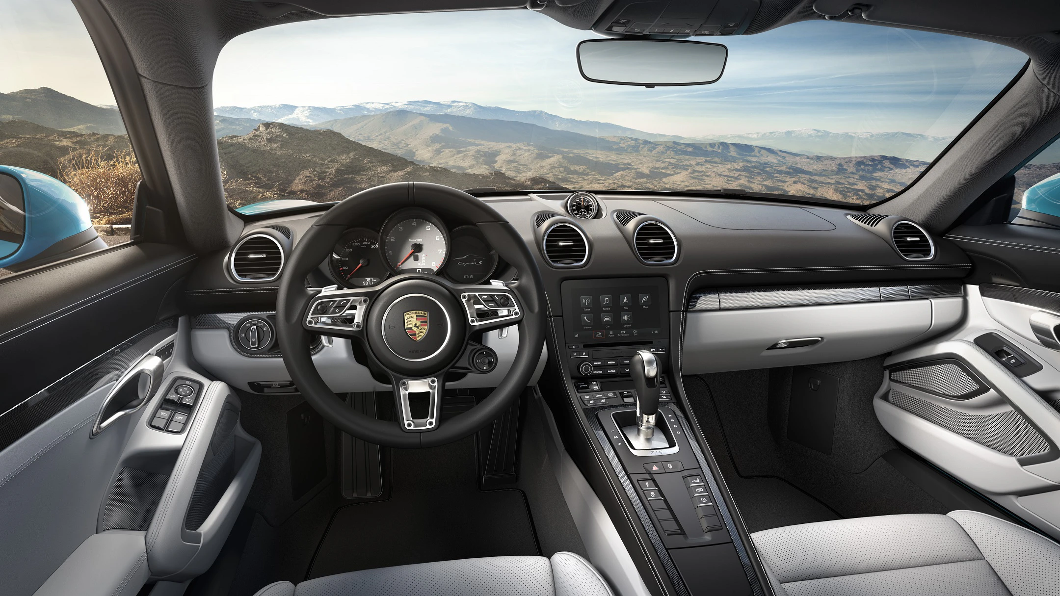 Innenraum eines Porsche-Sportwagens mit luxuriösem Design, Ledersitzen, moderner Instrumententafel und Panoramablick auf eine Berglandschaft.