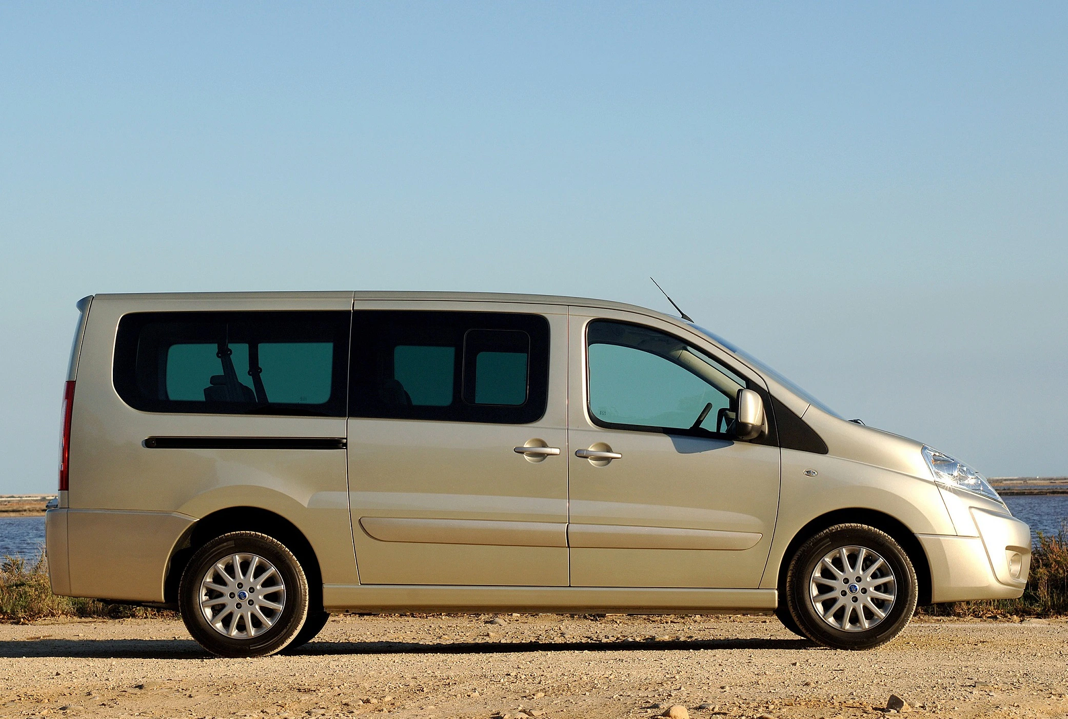 Beiger Minivan steht auf einem Feldweg mit klarem Himmel im Hintergrund, seitliche Ansicht.