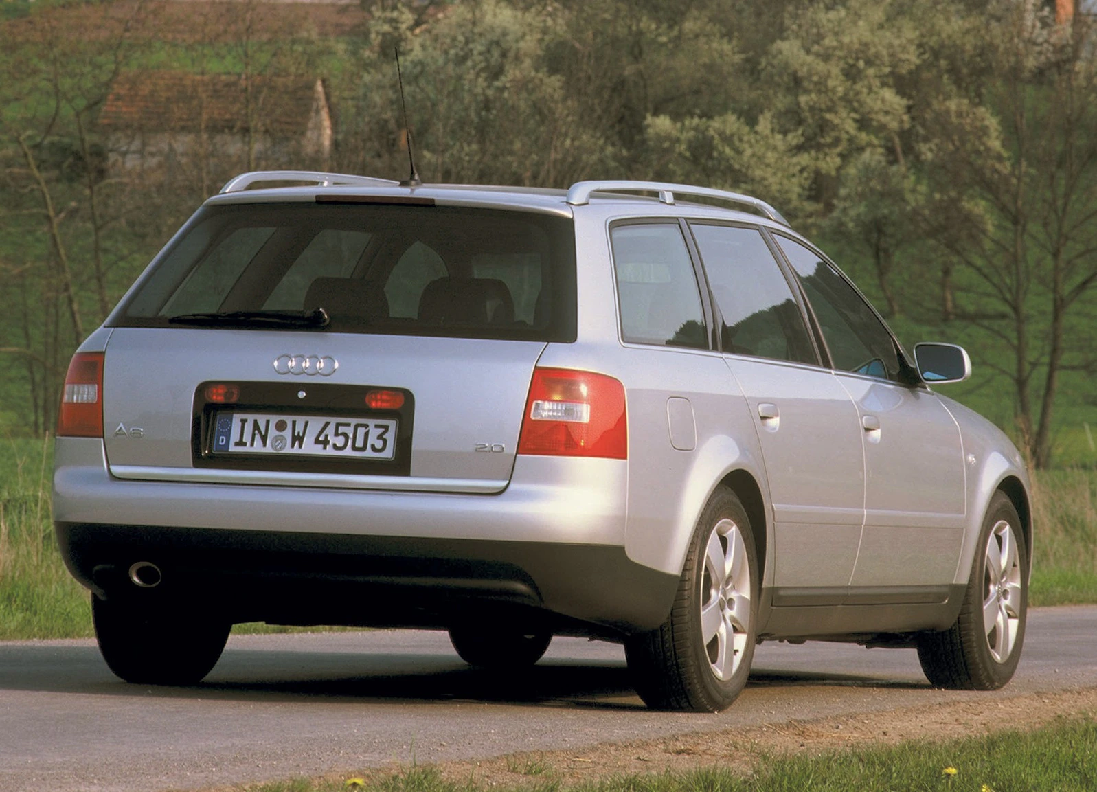 Silberner Audi A6 Avant auf einer ländlichen Straße, Rückansicht, geparkt, Bäume im Hintergrund.