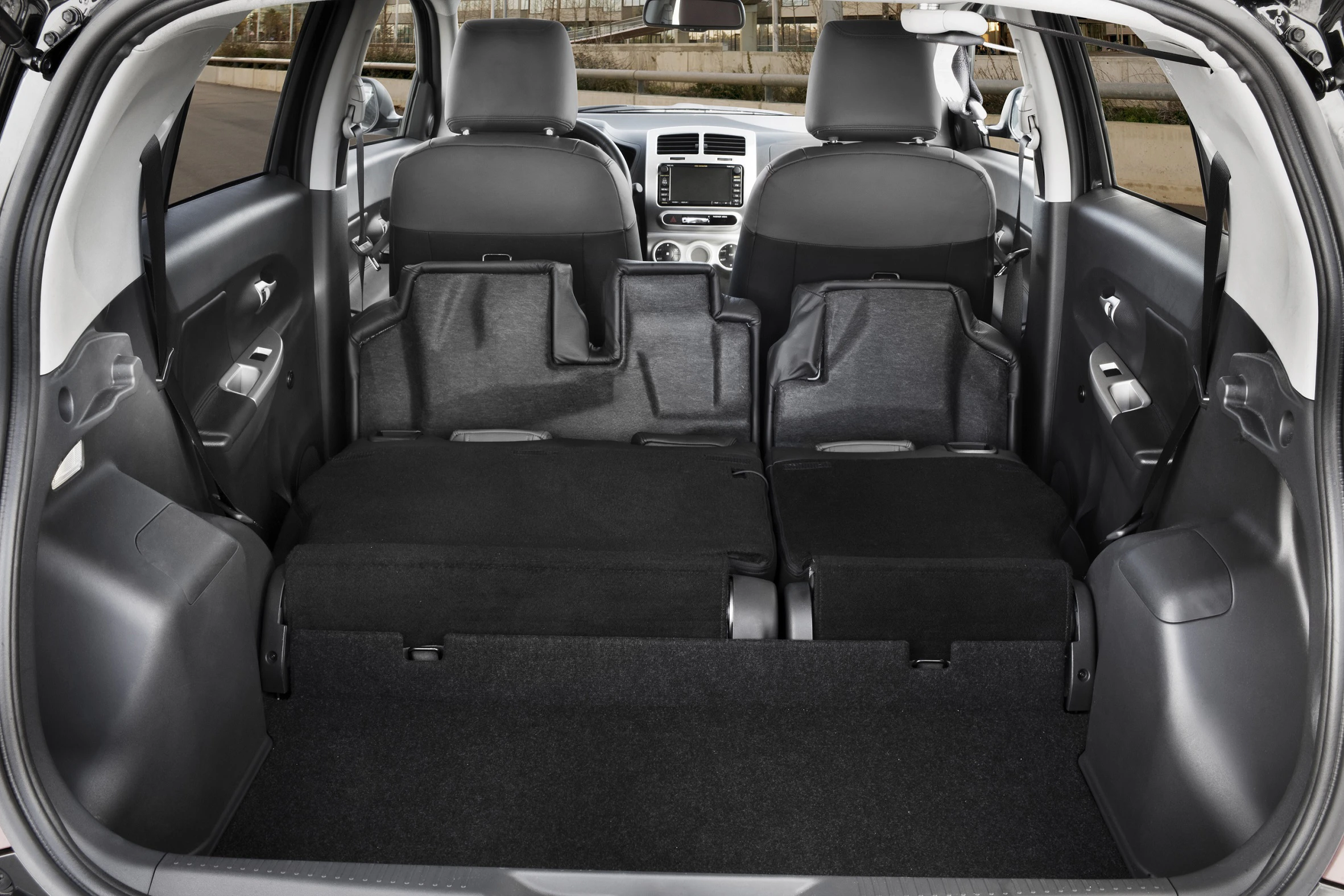 Innenraum eines Autos mit umgeklappten Rücksitzen, die eine große, flache Ladefläche bilden. Moderenes Armaturenbrett sichtbar.