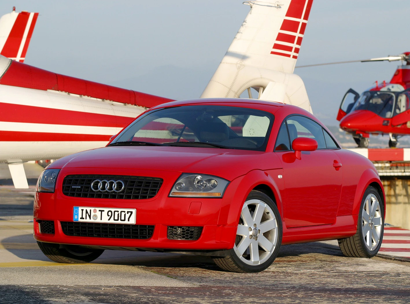 Roter Audi TT steht auf einem Flugplatz, im Hintergrund ein Hubschrauber und Propellerflugzeug.