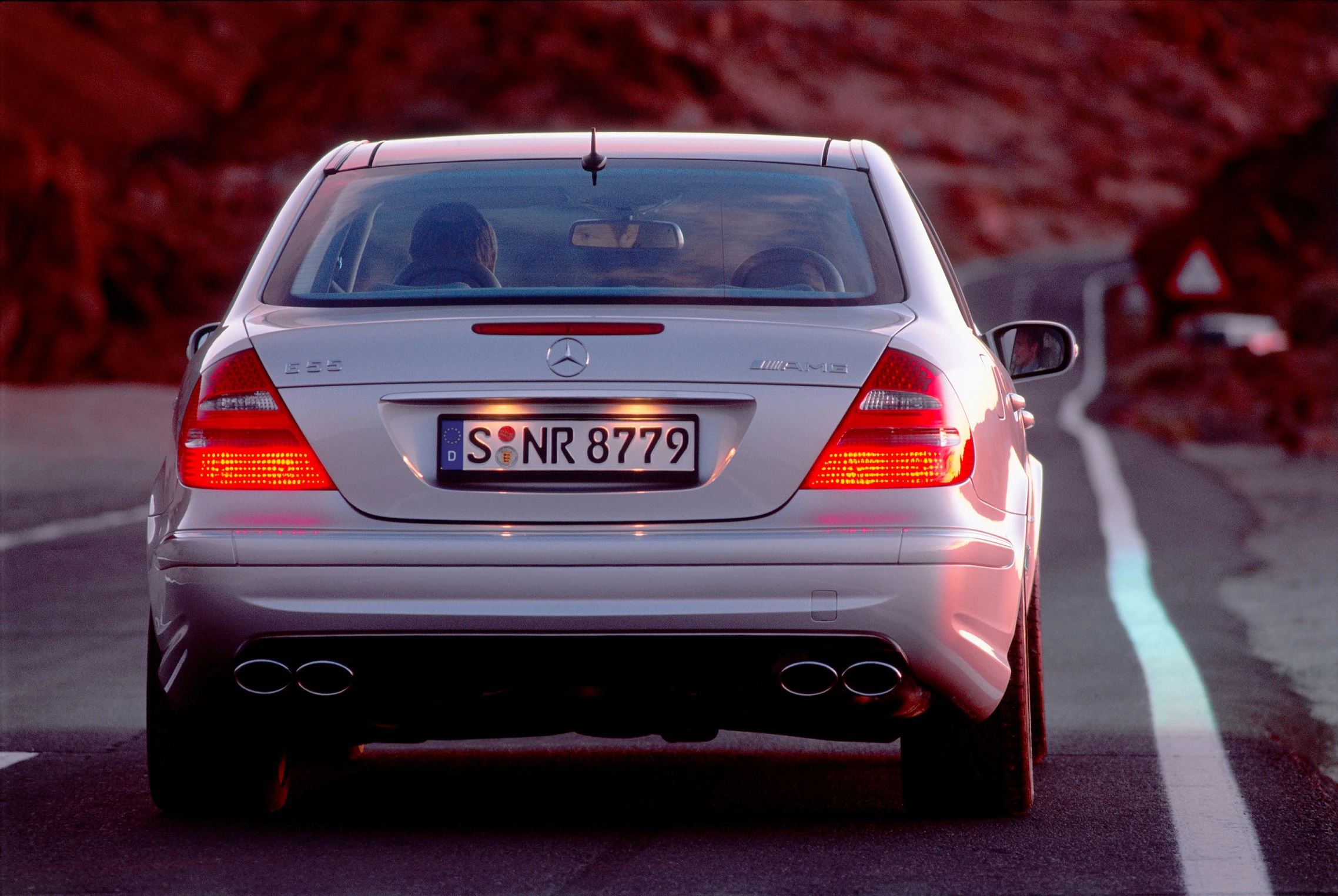 Silberner Mercedes-Benz C32 AMG auf einer Landstraße, von hinten sichtbar, bei Sonnenuntergang.