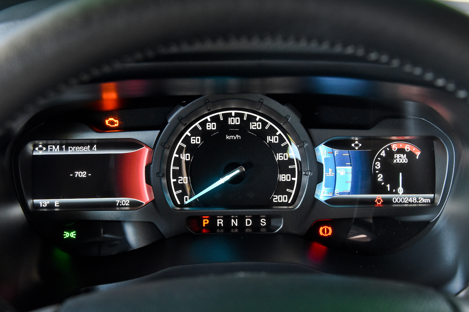 Armaturenbrett eines Autos mit Tacho, Drehzahlmesser, digitalen Anzeigen für Temperatur, Radio und Gangwahlhebel. Beleuchtete Kontrollleuchten.