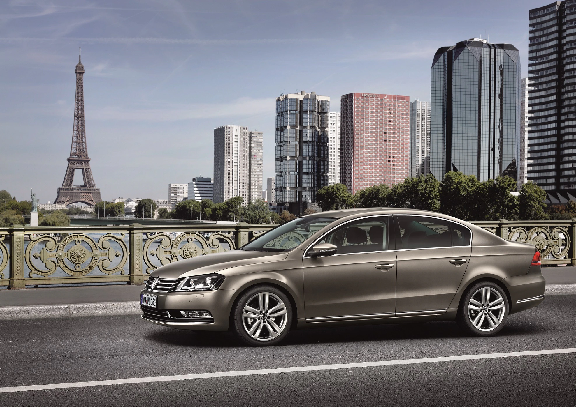 Ein brauner Volkswagen-Passat fährt auf einer Brücke in Paris. Im Hintergrund sind der Eiffelturm und moderne Hochhäuser zu sehen.