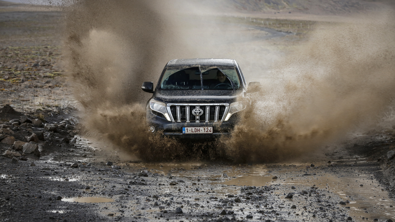 Ein schwarzer SUV fährt durch schlammiges Gelände und spritzt Wasser und Schlamm in die Luft.