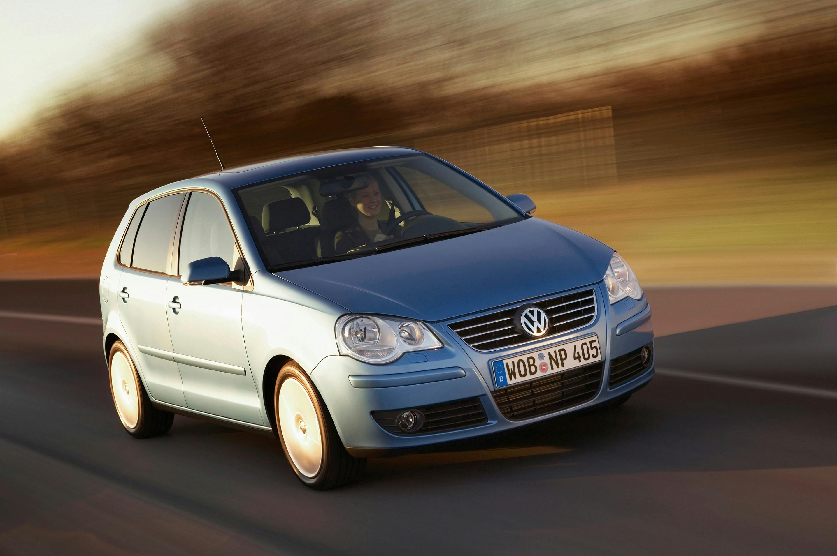 Blauer Volkswagen Polo fährt dynamisch auf einer Straße, unscharfer Hintergrund, deutet auf Geschwindigkeit und Bewegung hin.