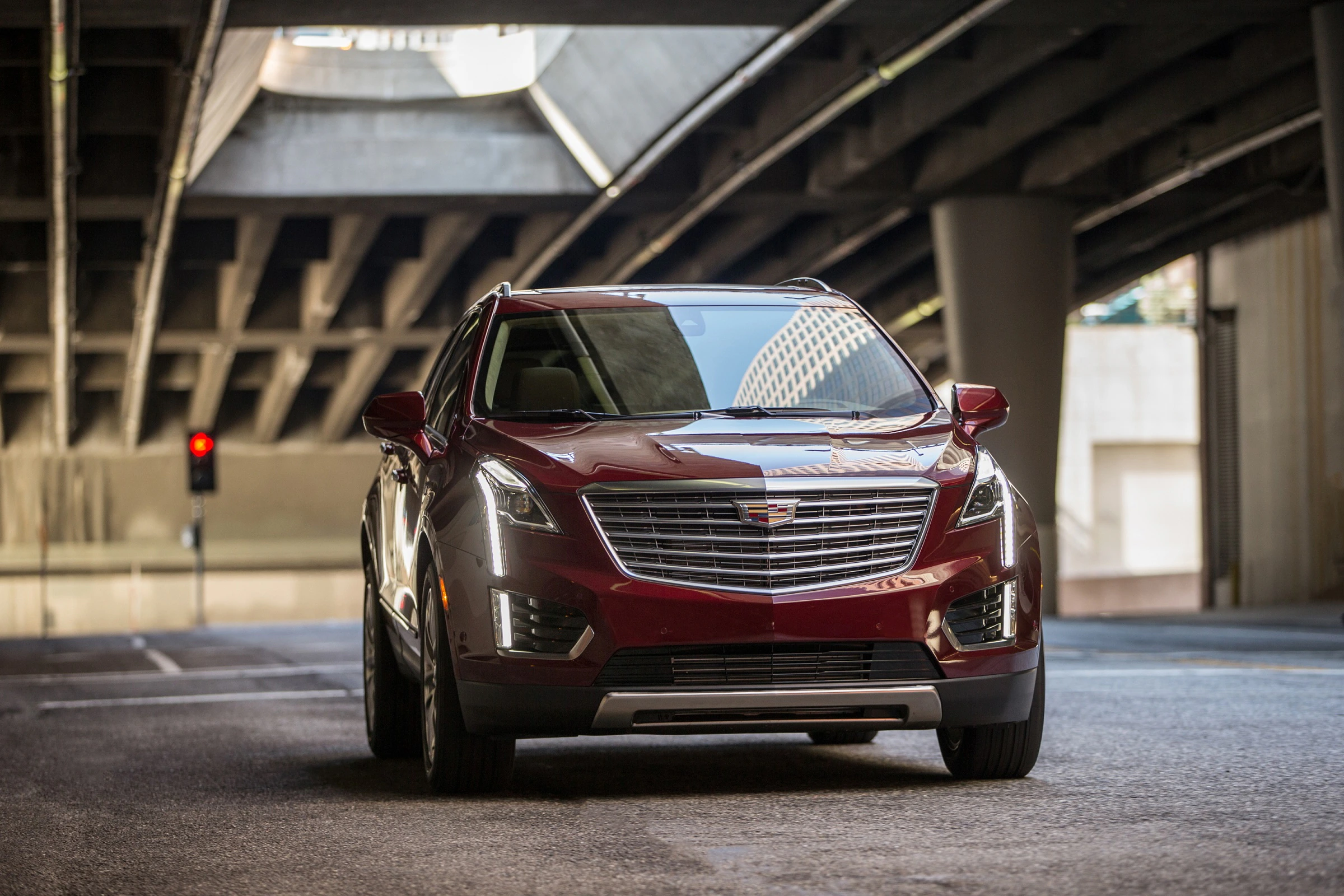Roter Cadillac-SUV steht auf einer Straße unter einer Betonüberführung mit roten Ampeln im Hintergrund.