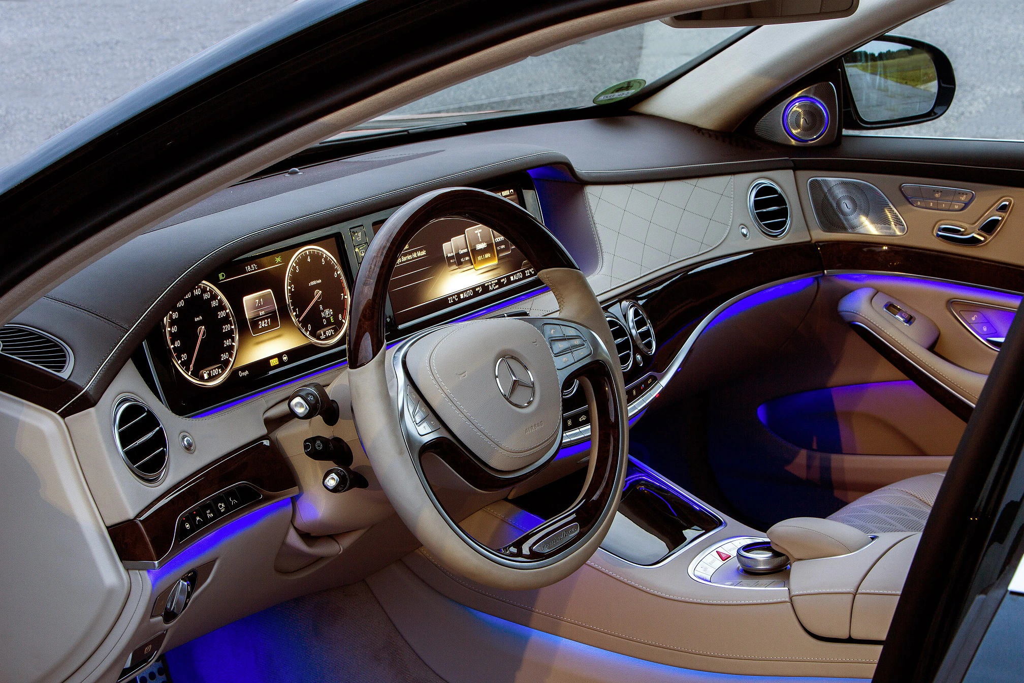 Innenraum eines Luxusautos mit beleuchtetem Armaturenbrett, lederbezogenem Lenkrad und moderner Anzeige, blau und beige Akzente.