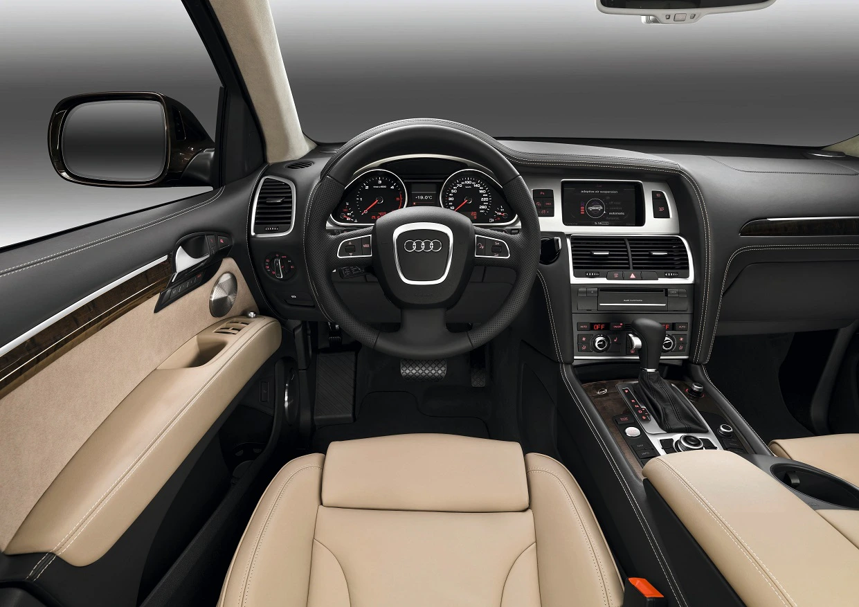 Innenraum eines Audi mit beigem Leder, Lenkrad mit Audi-Logo, Armaturenbrett mit Tacho, Mittelkonsole und Infotainment-Bildschirm.