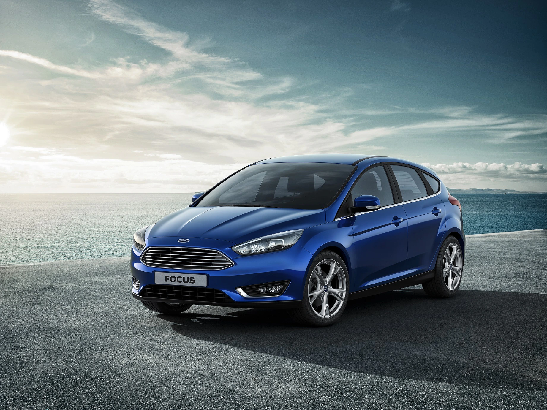 Blauer Ford Focus auf einer Küstenstraße bei sonnigem Wetter, mit Meerblick im Hintergrund.