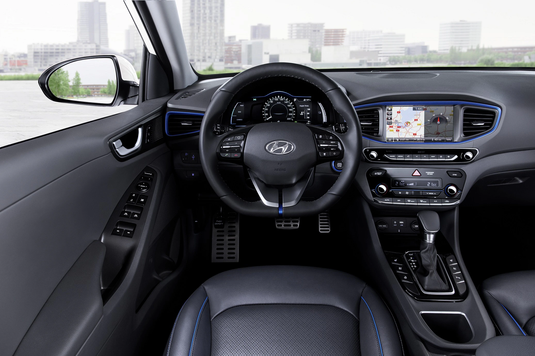 Innenraum eines modernen Autos mit Fokus auf das Lenkrad, Armaturenbrett und Navigationsdisplay. Stadtansicht durch die Windschutzscheibe.