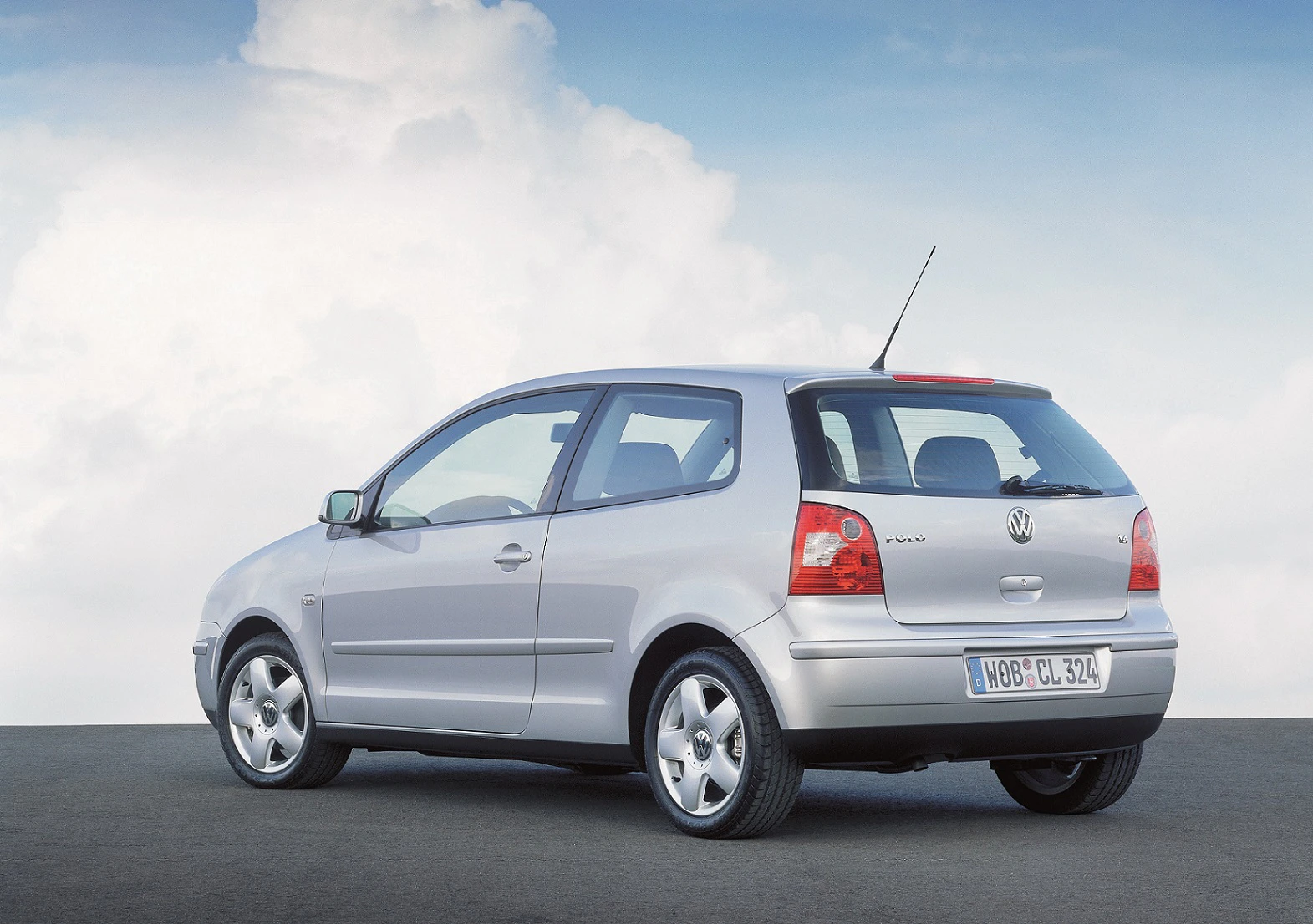 Silberner Volkswagen Polo vor einem blauen Himmel mit Wolken, aus der hinteren linken Perspektive fotografiert.