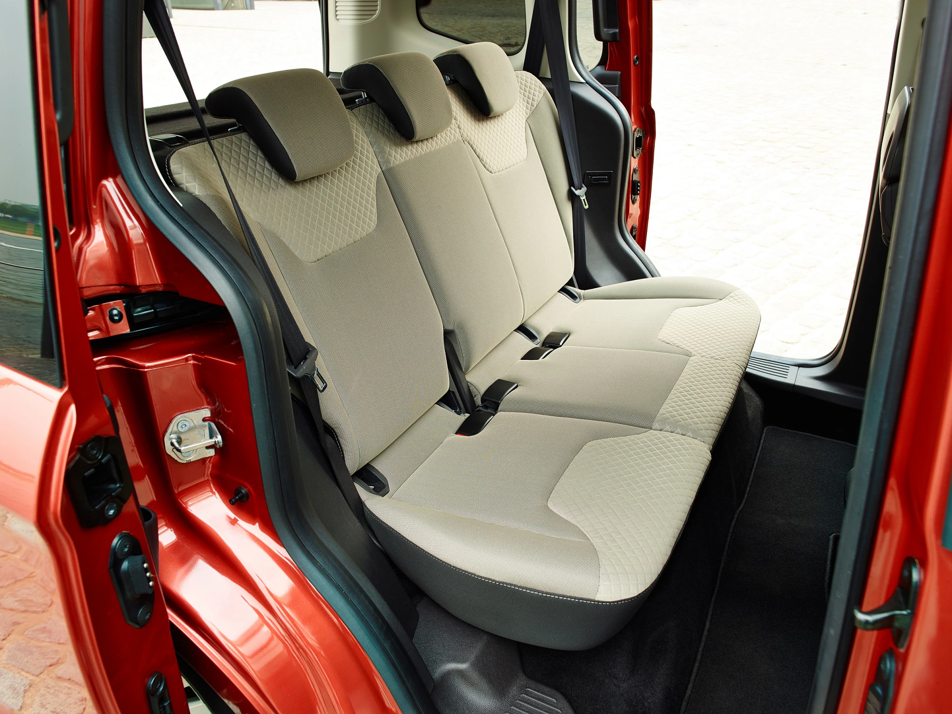 Rückansicht eines roten Autos mit beige Stoffrücksitzen, offenem hinteren Seiteneingang und sichtbaren Kopfstützen.