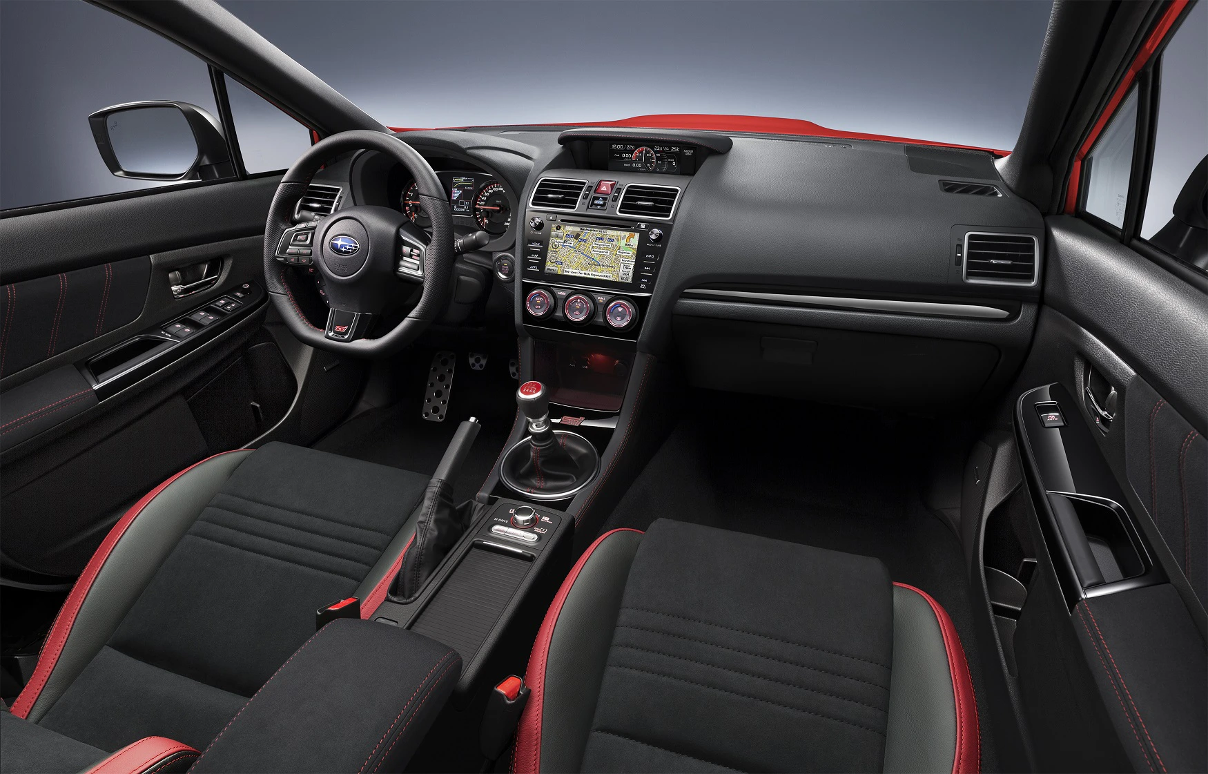 Innenraum eines modernen Autos mit schwarzem und rotem Interieur, Lenkrad links, Infotainment-Bildschirm und manuellem Schaltknauf.