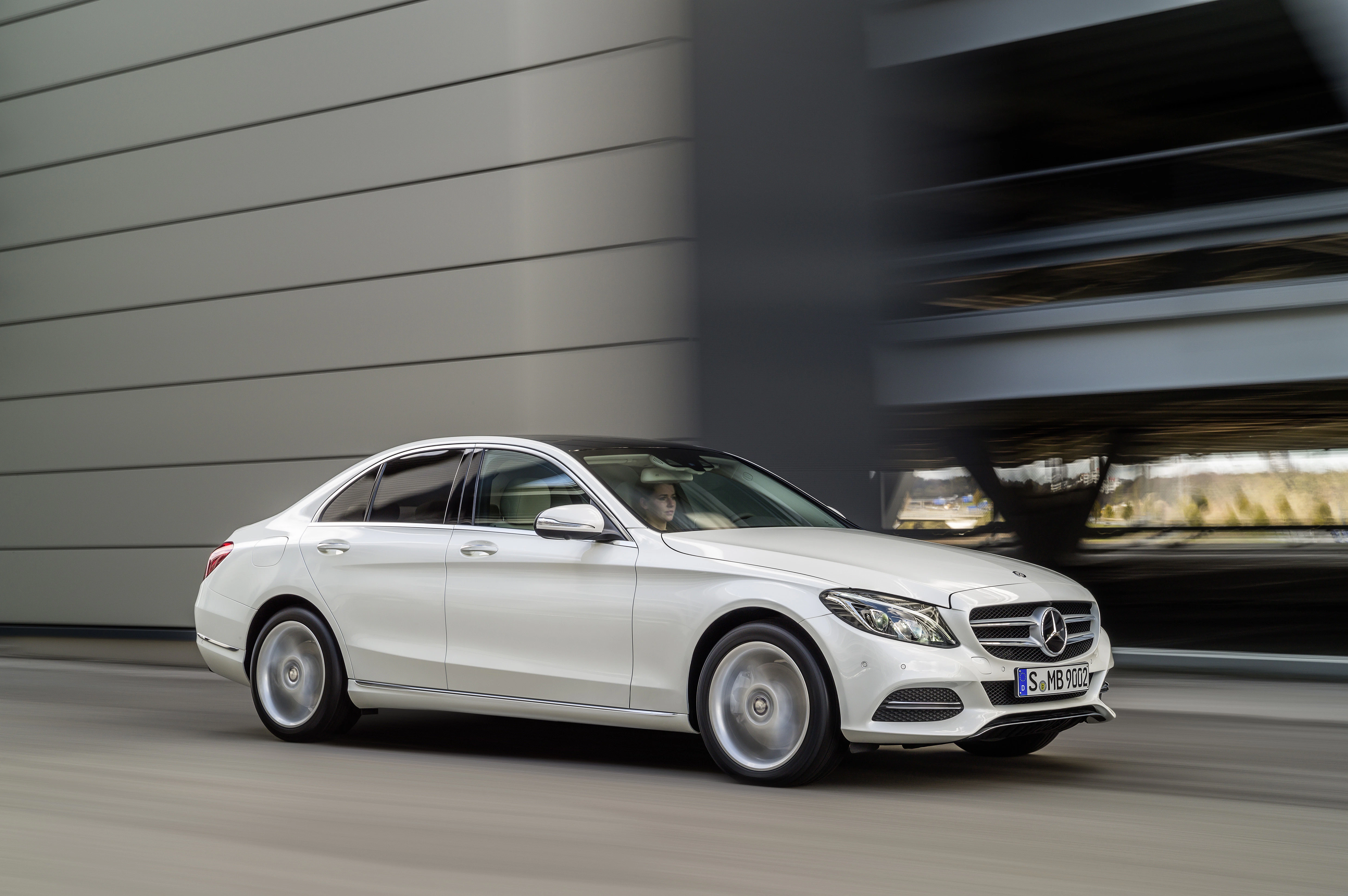 Weiße Mercedes-Limousine fährt dynamisch auf einer Straße vor einem modernen Gebäude.